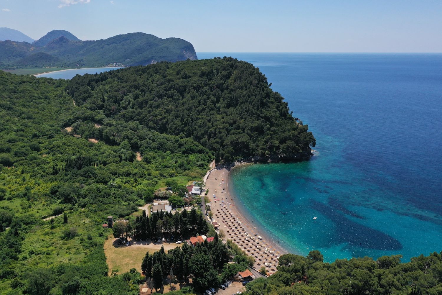 Luftaufnahme des Strandes Lučice und der Küste von Petrovac, Montenegro: azurblaues Meer, dichter Wald und Feriengebiet.