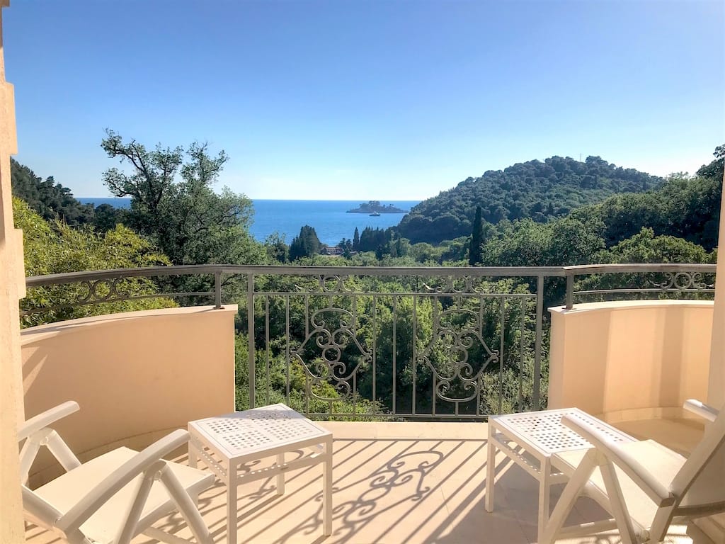 Balkon mit schmiedeeinfachem Geländer und Möbeln in einer Wohnung in Petrovac, Montenegro, mit Panoramablick auf das Meer und das Grün.