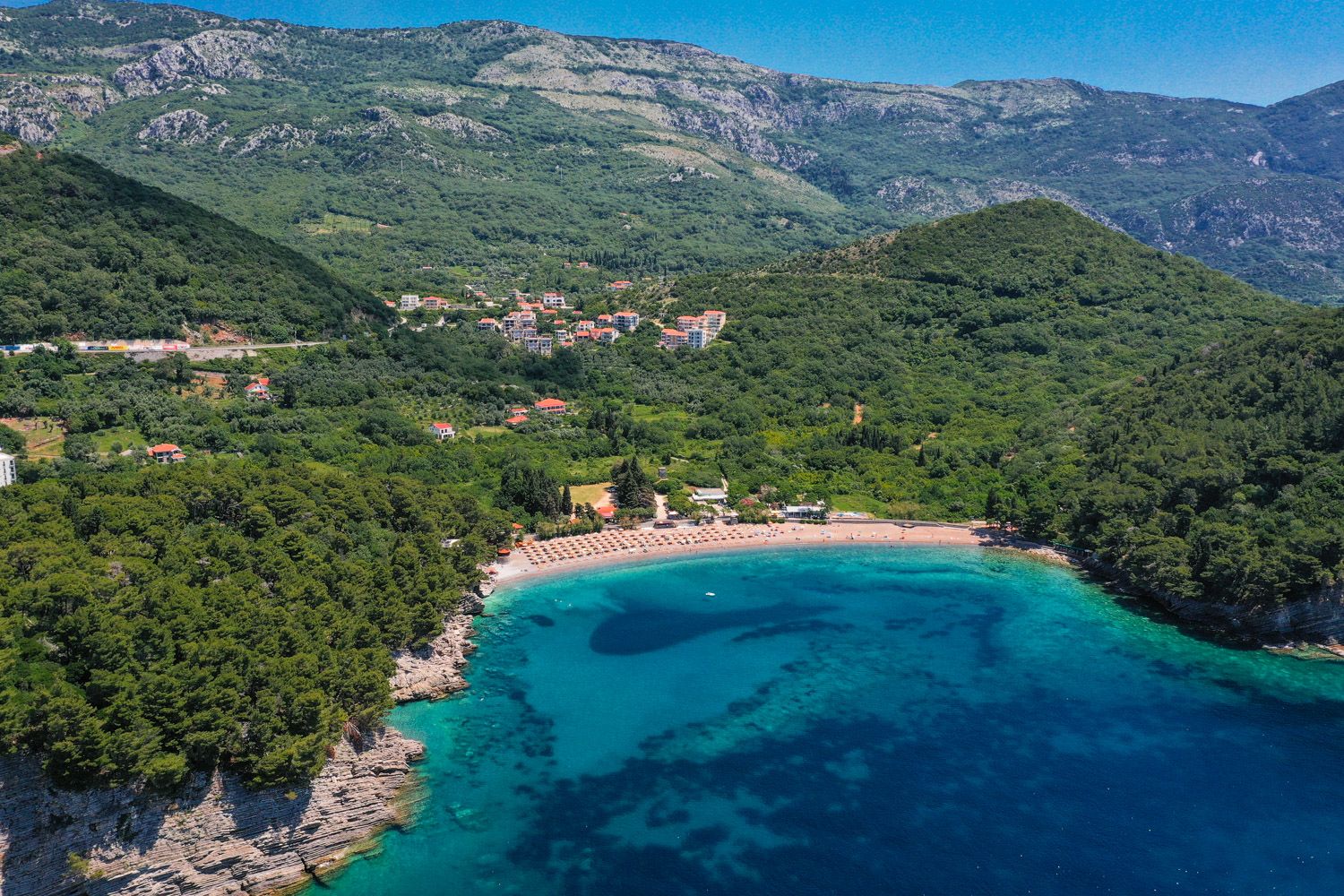 Panoramablick auf den Strand Lucice und die grünen Berge in Petrovac, Montenegro: malerische Bucht mit azurblauem Wasser und Wald.