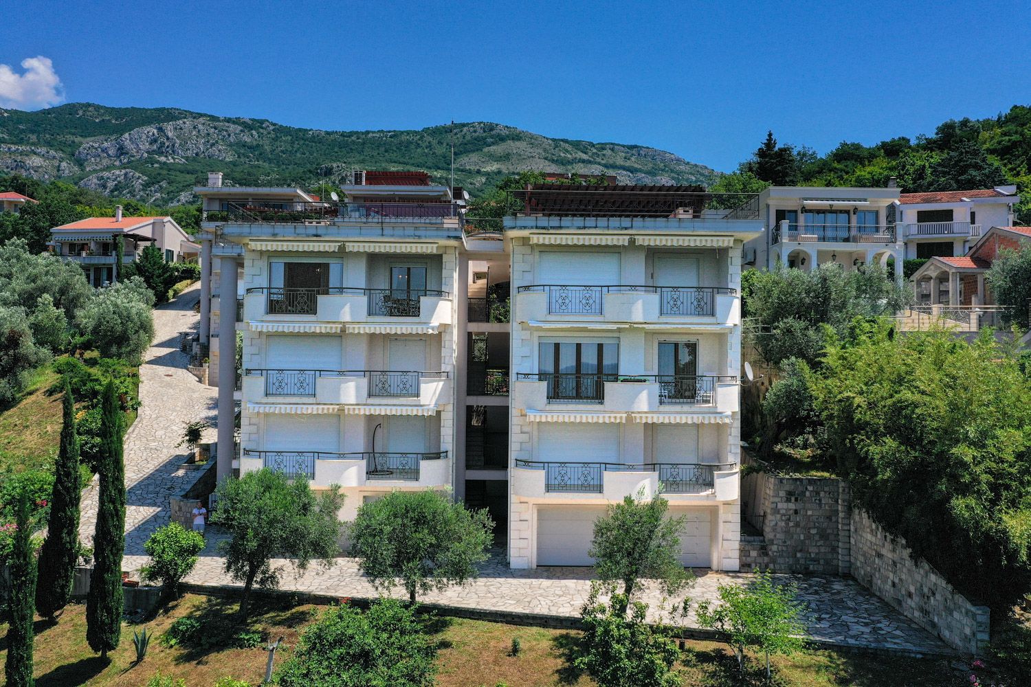 Dreistöckige Villa mit Balkonen und Terrassen in Petrovac, Montenegro: Blick auf die Fassade des Gebäudes inmitten von Grün und Bergen.