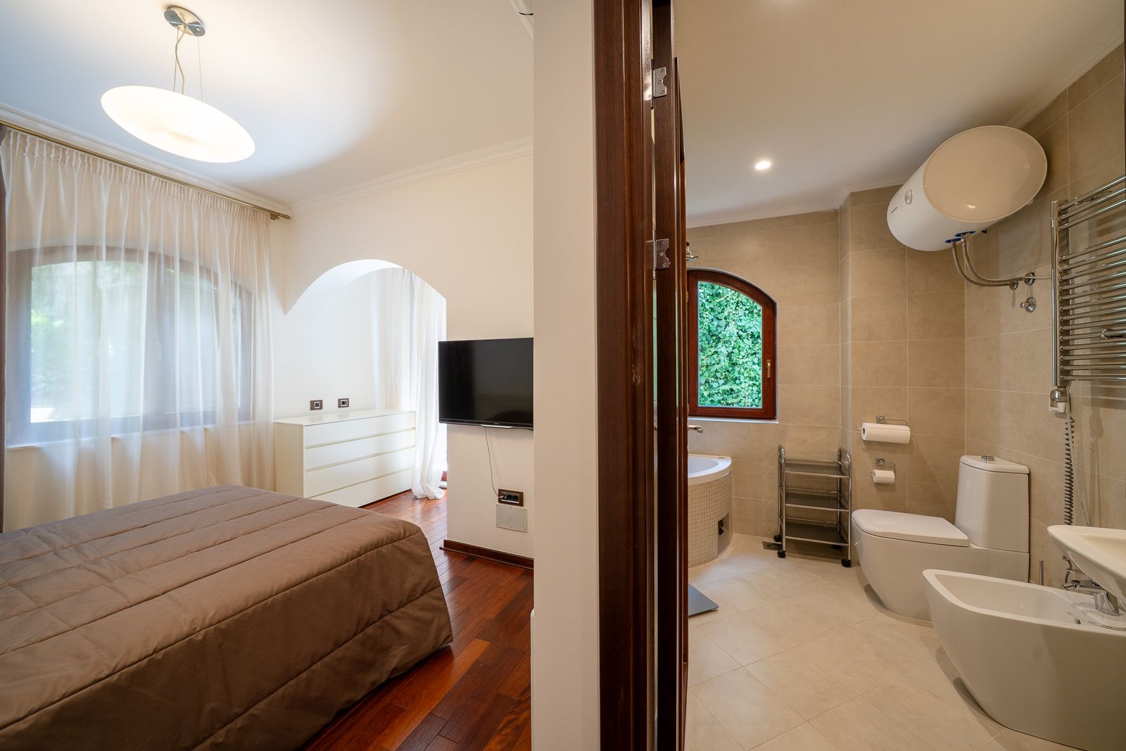 Innenansicht von Schlafzimmer und Badezimmer in einer Wohnung, Petrovac, Montenegro: Doppelbett, TV und moderne Sanitäranlagen.
