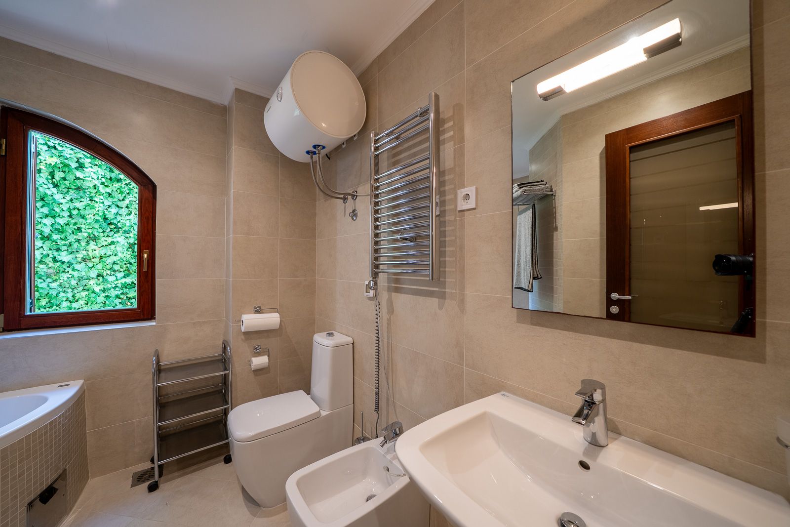 Modernes Badezimmer in einer Wohnung in Petrovac, Montenegro: weiße Sanitärkeramik, Bidet, Spiegel und Fenster mit Blick ins Grüne.