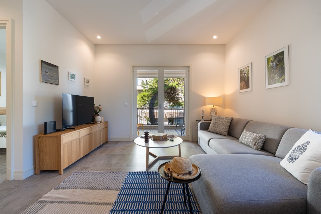Modernes Wohnzimmer in der Wohnung Lustica Bay, Tivat, Montenegro: graues Sofa, Holzkommode und Zugang zum Balkon.