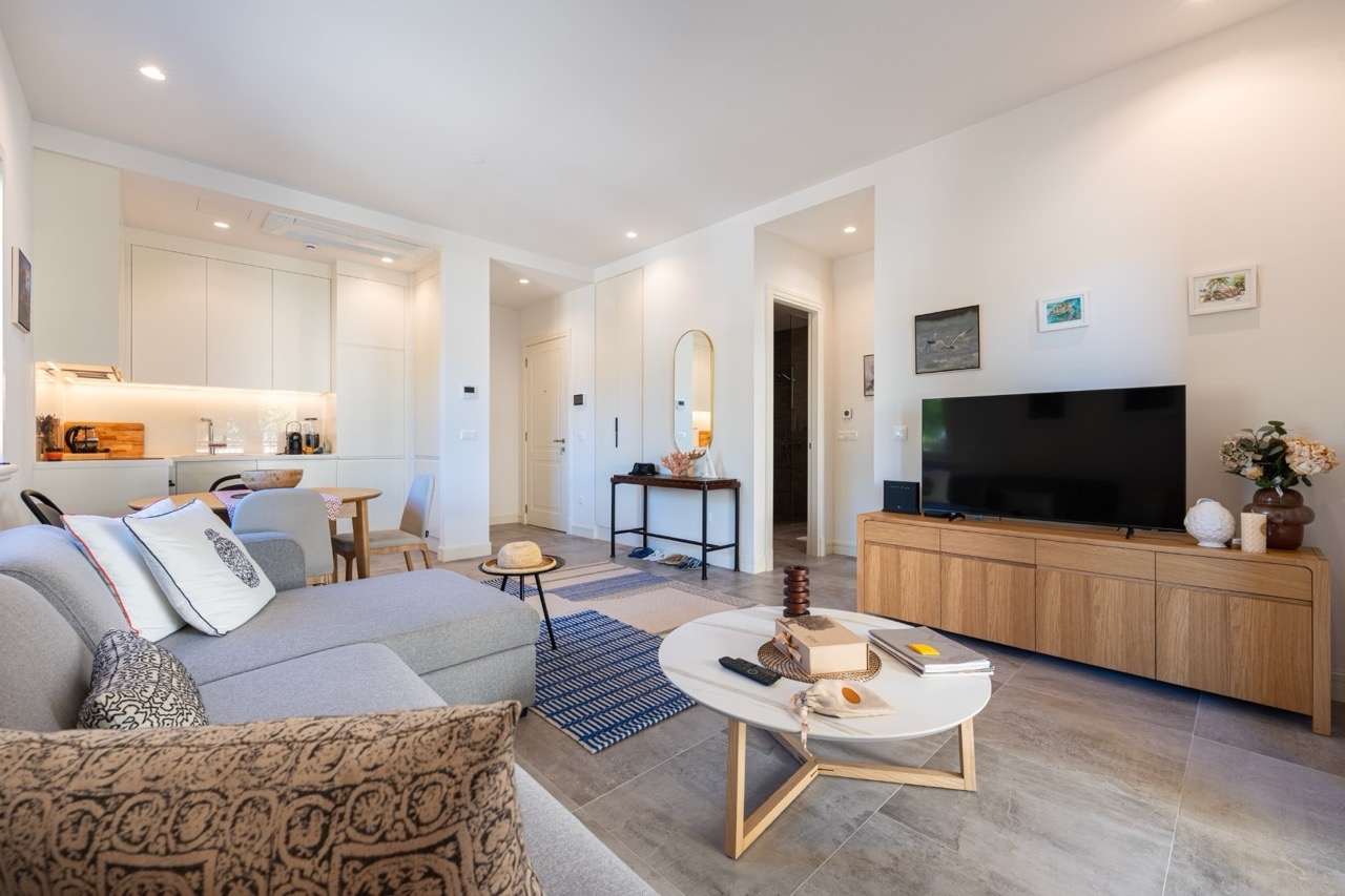 Modernes Wohnzimmer mit Küche in der Wohnung Luštica Bay, Tivat, Montenegro: helles Interieur, weiche Möbel und TV-Bereich.