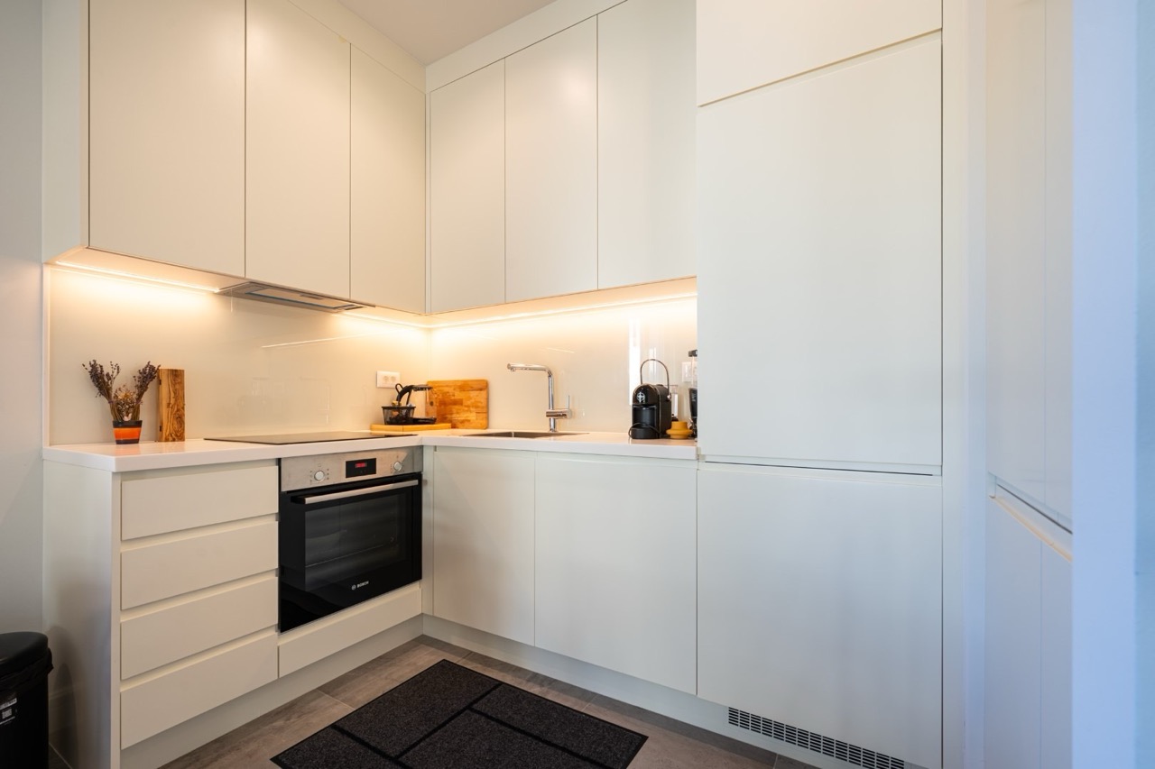 Moderne weiße Küche in einer Wohnung im ЖК Luštica Bay, Tivat, Montenegro: Einbaugeräte und Arbeitsplattenbeleuchtung.