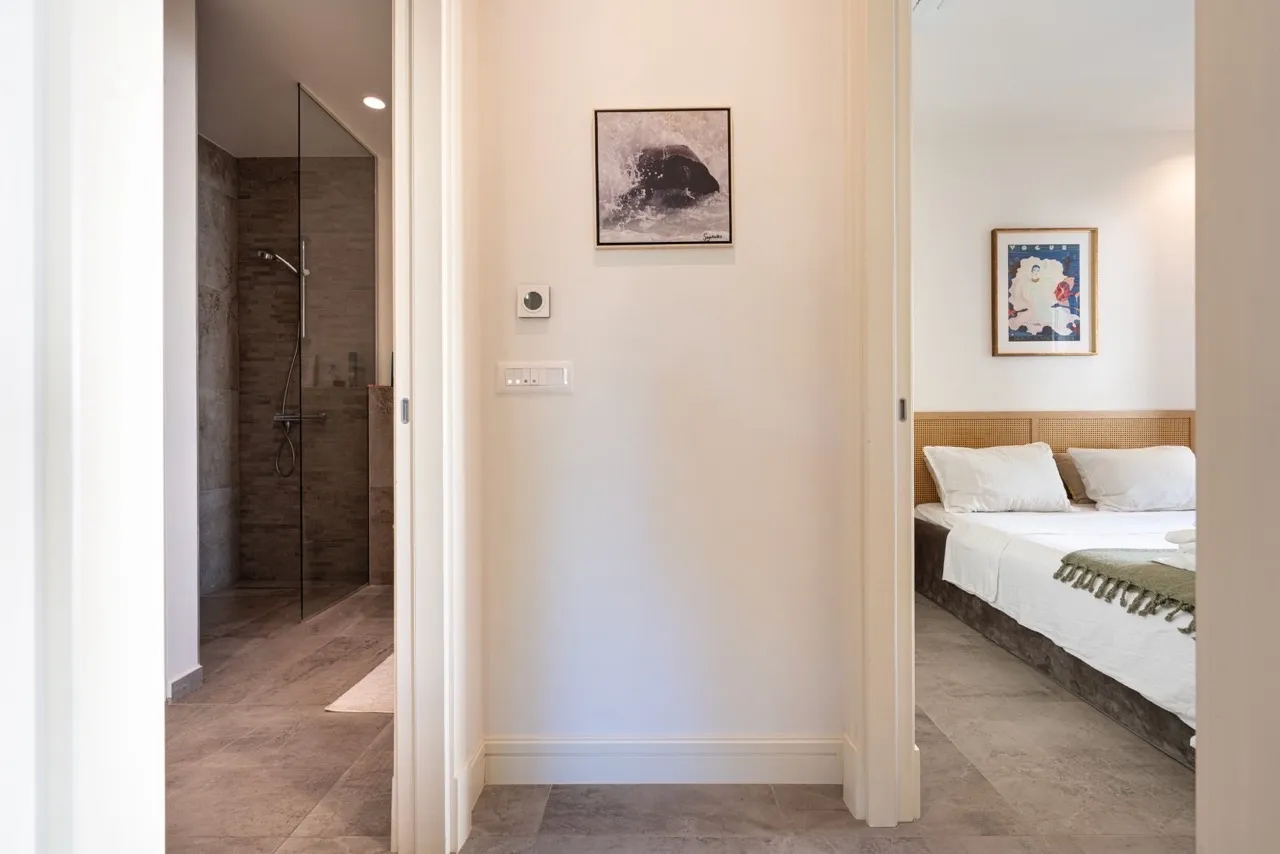 Flurblick mit Sicht auf ein Schlafzimmer und ein Badezimmer mit Glasdusche.