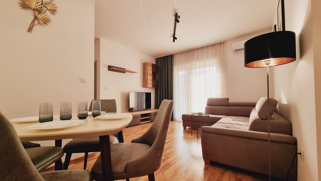 Savremeni dnevni boravak sa trpezarijom u stanu u Bečićima, Crna Gora: mekana sofa, stilizovan nameštaj i parket.