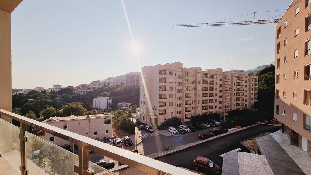 Pogled sa balkona stana u Bečićima, Crna Gora: panorama stambenog kompleksa, planinski pejzaž i parking ispred zgrade.