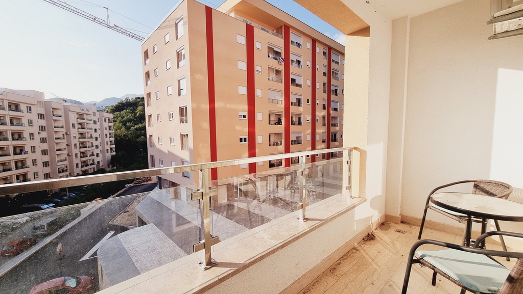 Balkon sa pletenim nameštajem i staklenom ogradom u stanu, grad Bečići, Crna Gora, pogled na stambeni kompleks.