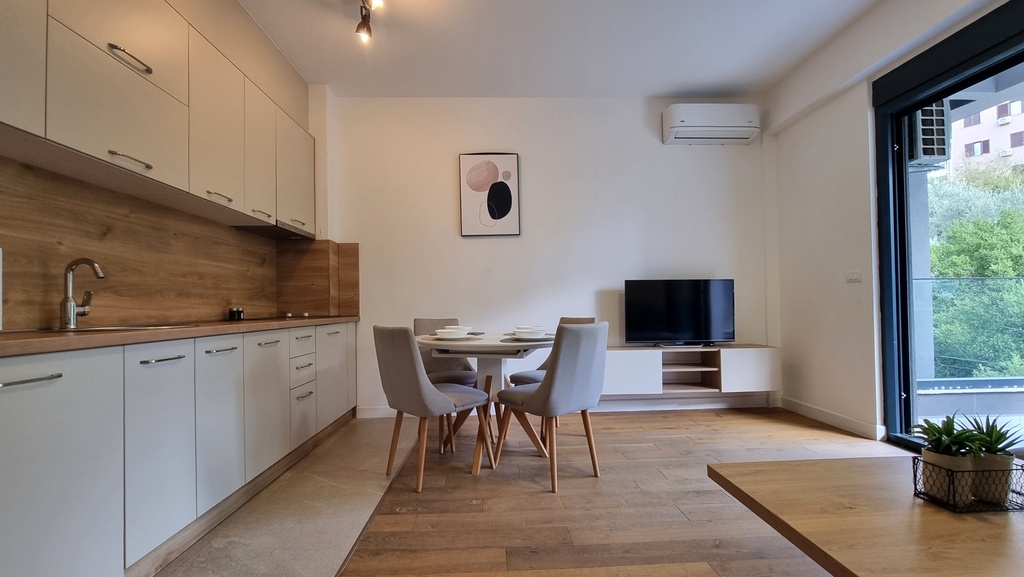 Modern kitchen-living room in an apartment in Bečići, Montenegro: light-colored furniture, dining area, and access to the terrace.