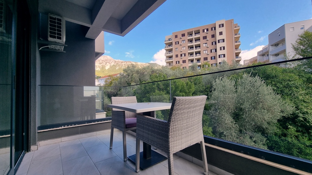 Balcony of a modern apartment in Bečići, Montenegro, with wicker chairs, a glass railing, and mountain views.
