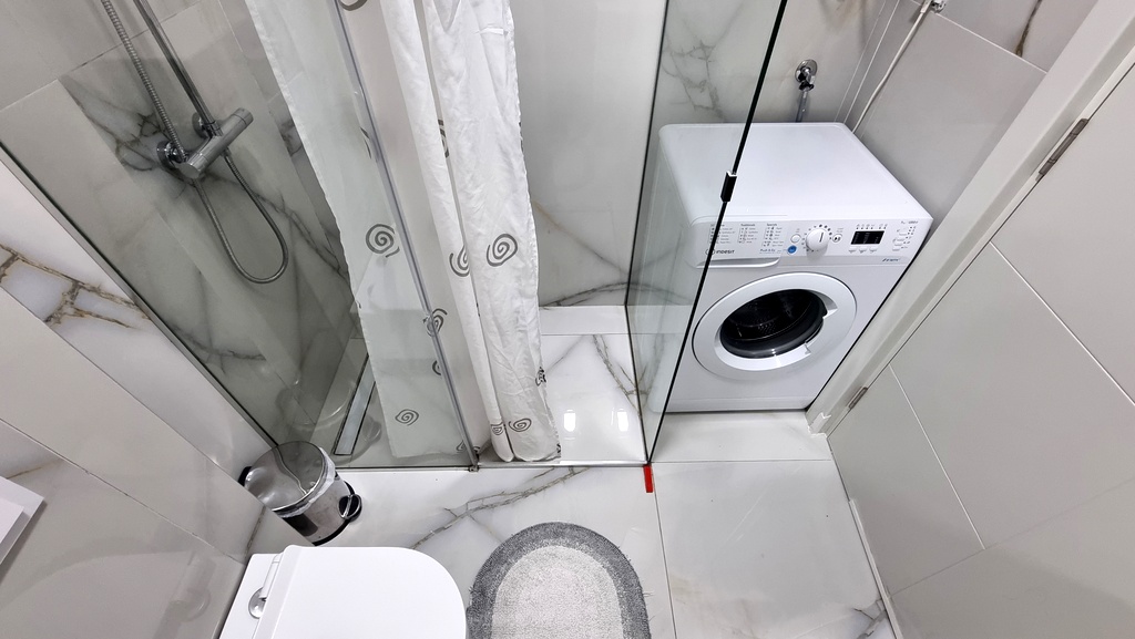 Modern bathroom in an apartment in Bečići, Montenegro: shower cabin, washing machine, and light-colored tiles.