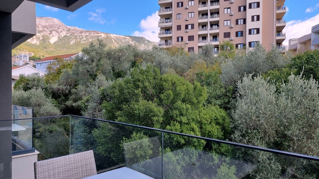 View from the apartment balcony in Bečići, Montenegro: a panorama of mountains, olive trees, and a modern residential complex.