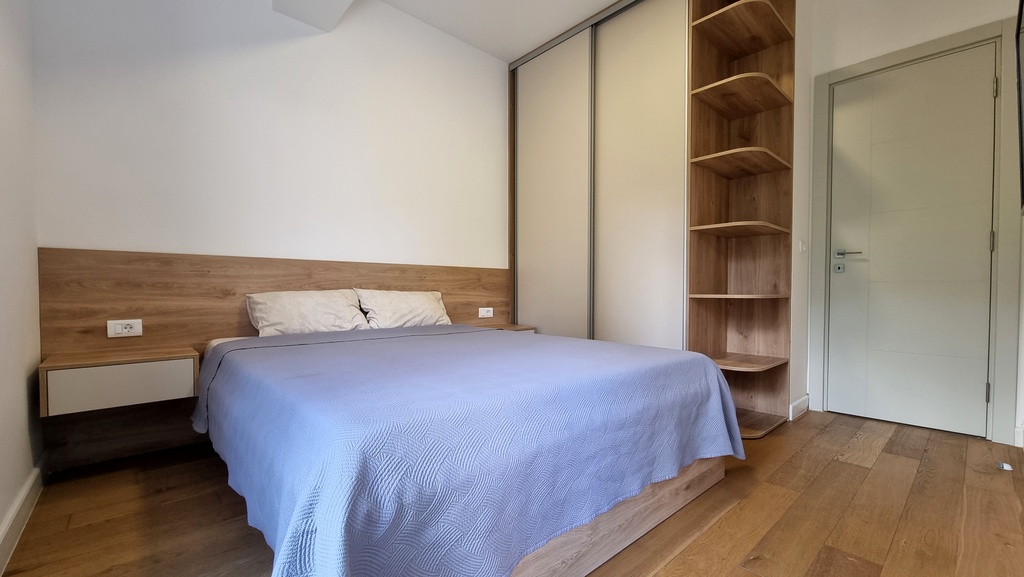 Modern bedroom in an apartment in Bečići, Montenegro: double bed, built-in wardrobe, and wood finishes.