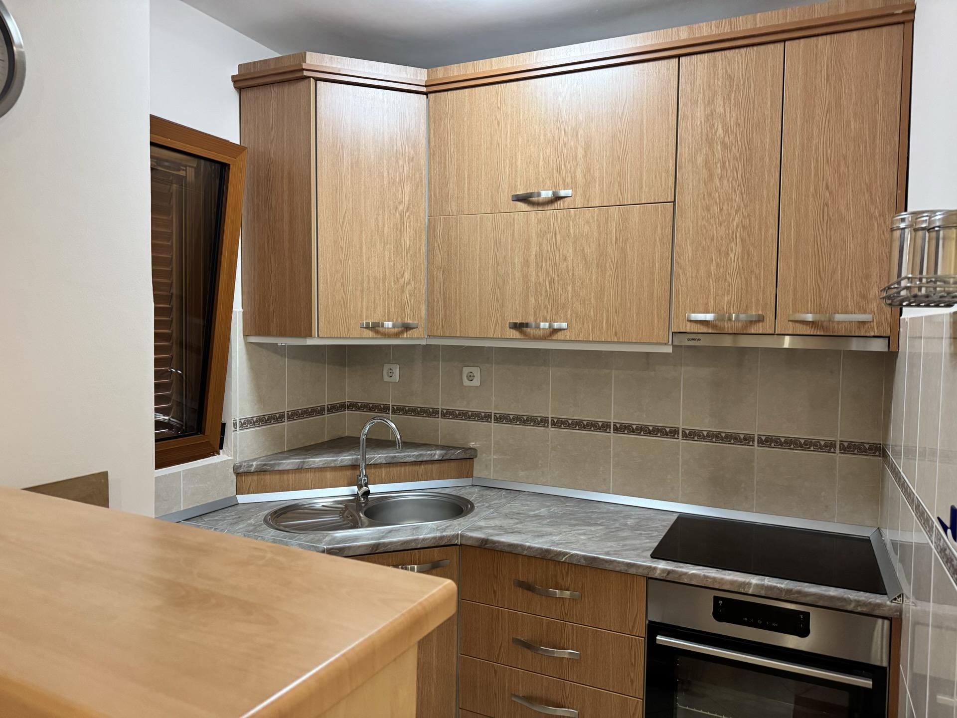 Eckküche in einer Wohnung in Budva, Montenegro: Holzfronten, eingebautes Kochfeld, Spüle und Arbeitsplatte in Marmoroptik.