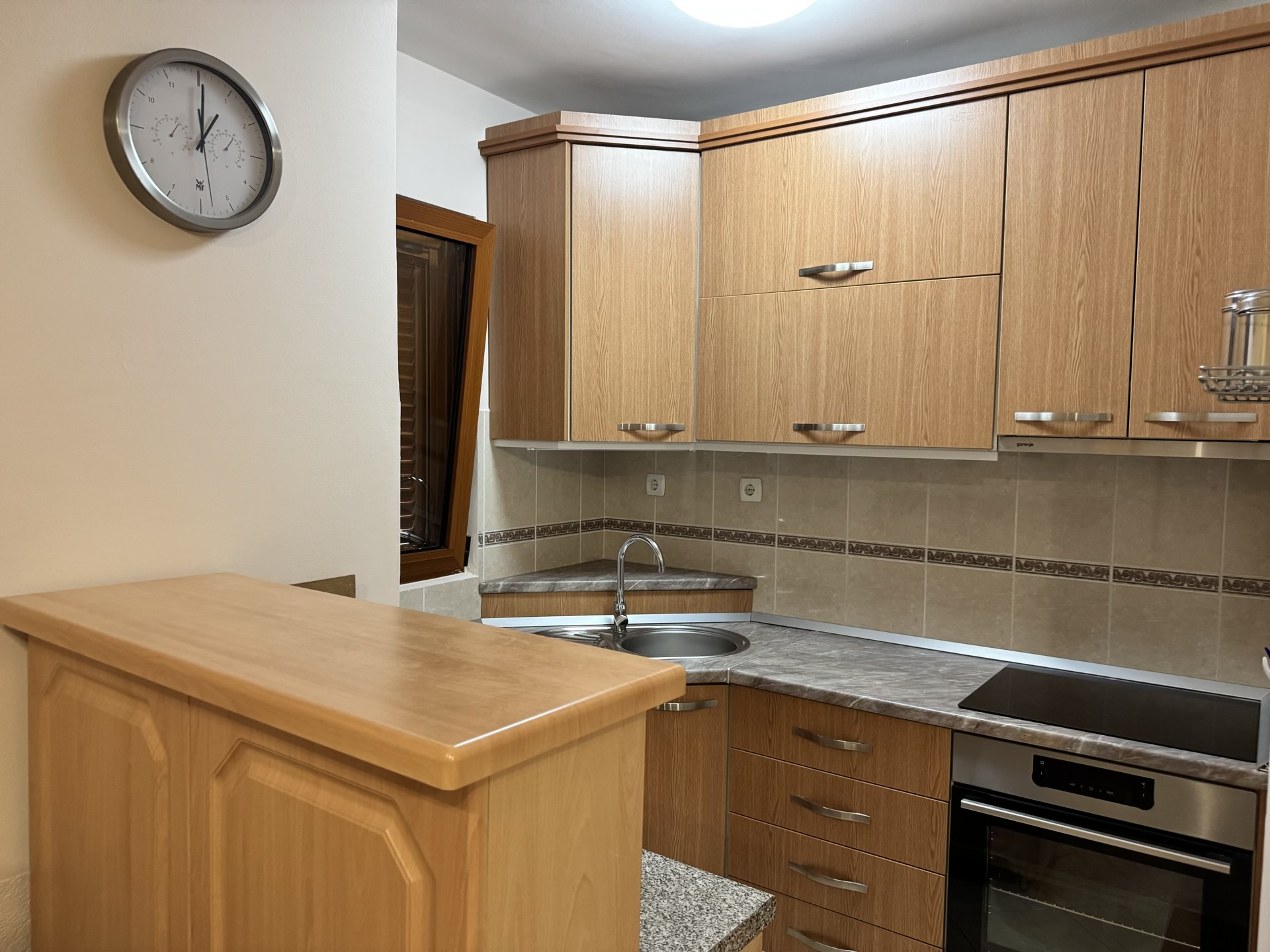 Eckküche mit Holzfronten und Bartheke in einer Wohnung, Budva, Montenegro. Einbaugeräte und Fliesen.