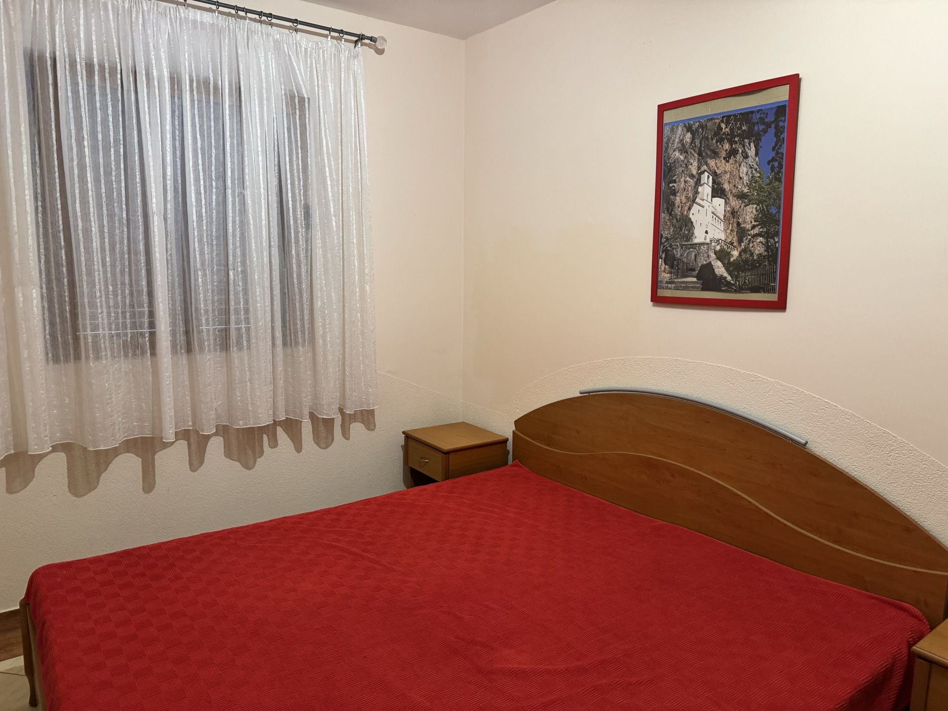 Schlafzimmer in einer Wohnung in Budva, Montenegro: Doppelbett mit Holz-Kopfteil, Nachttische und ein Bild an der Wand.