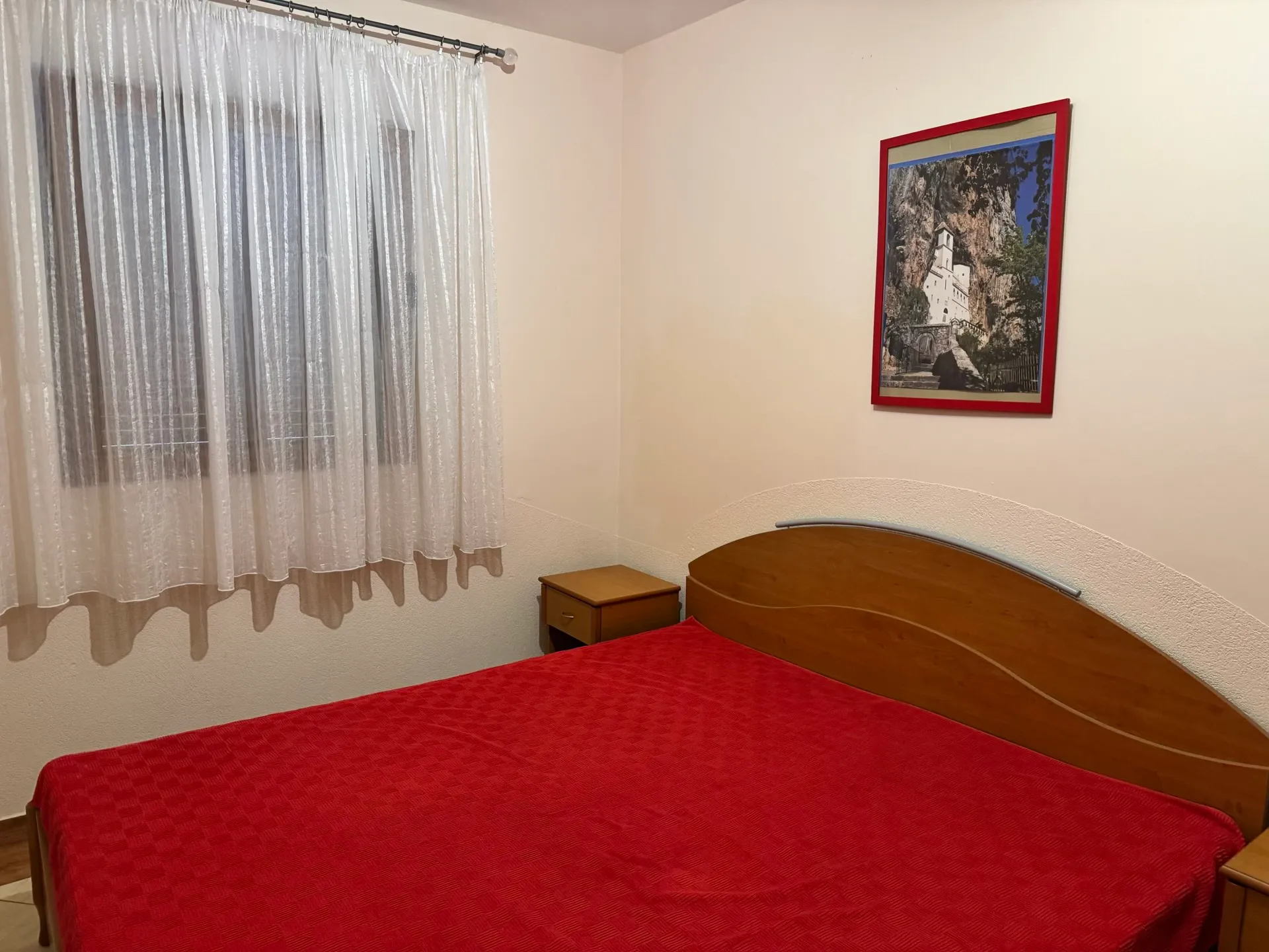 Bedroom in an apartment in Budva, Montenegro: a double bed with a wooden headboard, bedside tables, and a painting on the wall.