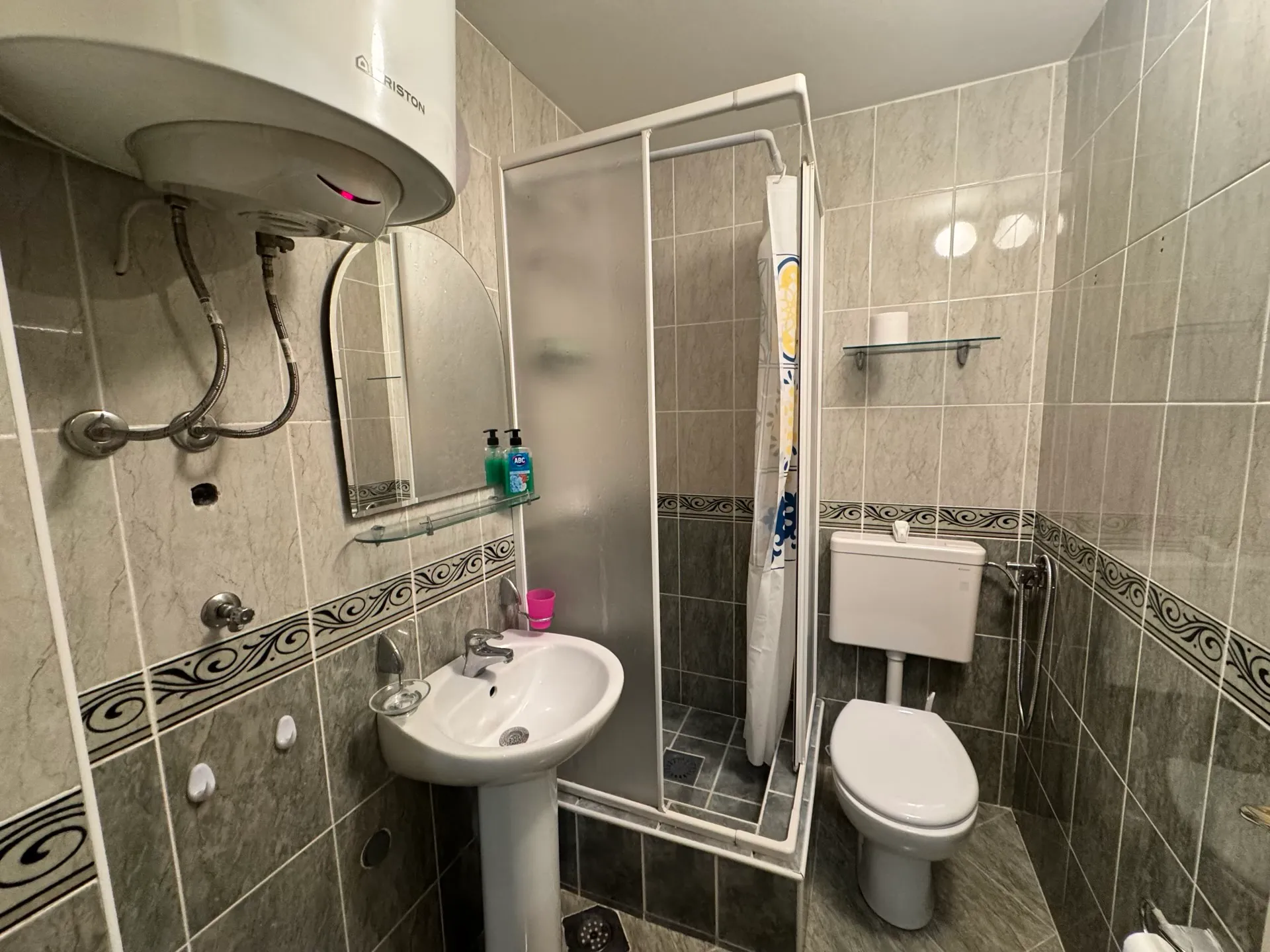 Bathroom in an apartment in Budva, Montenegro: shower cabin, sink, toilet, and an Ariston boiler on the wall.
