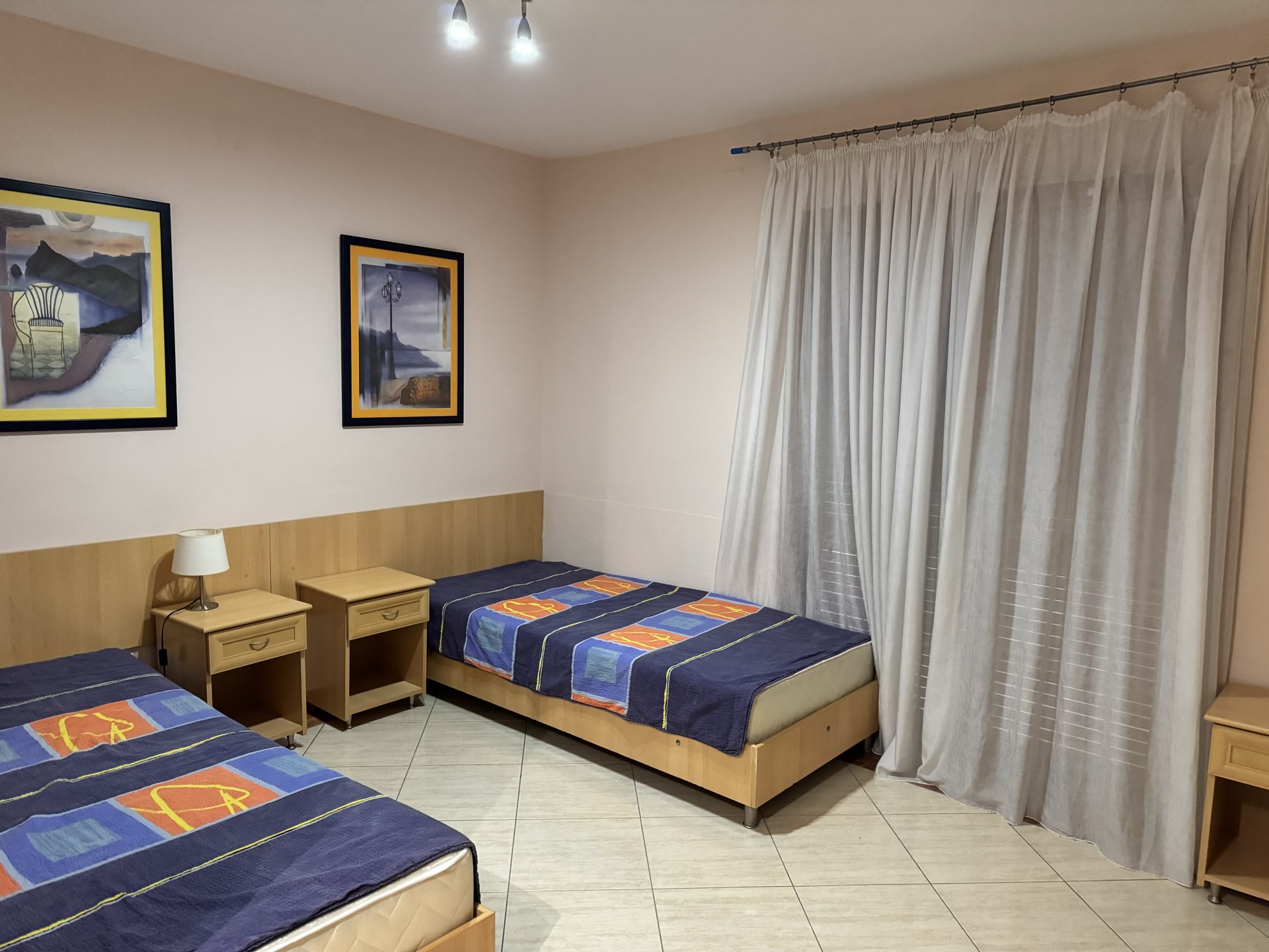 Schlafzimmer mit zwei Einzelbetten in einer Wohnung in Budva, Montenegro: helle Möbel, Bilder und bodentiefe Vorhänge.