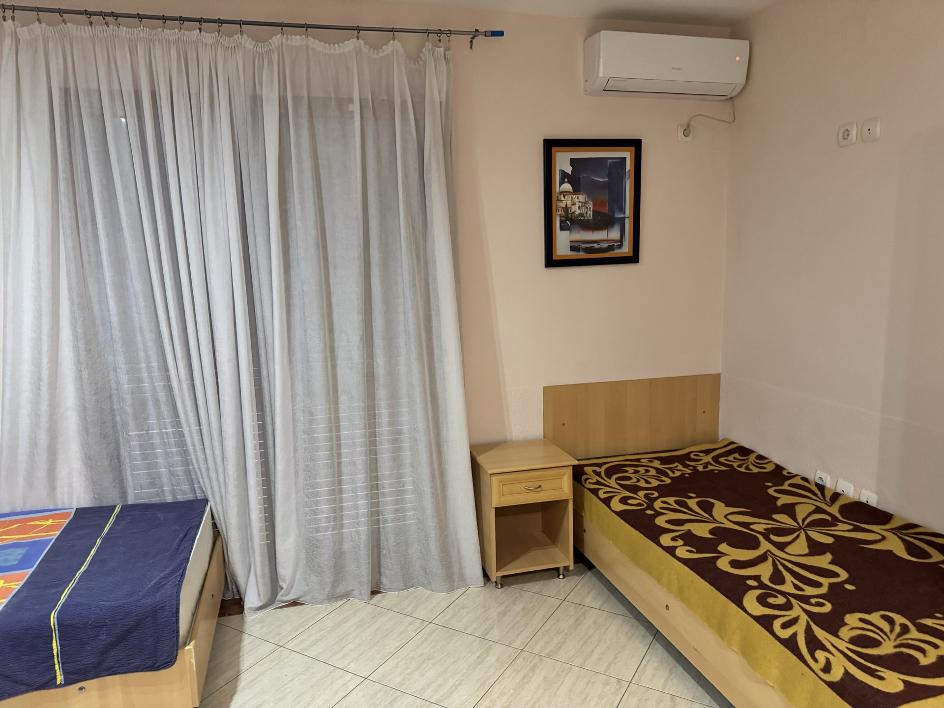 Schlafzimmer in einer Wohnung in Budva, Montenegro: zwei Betten, Nachttisch, helle Wände, Klimaanlage und Panoramagardinen.