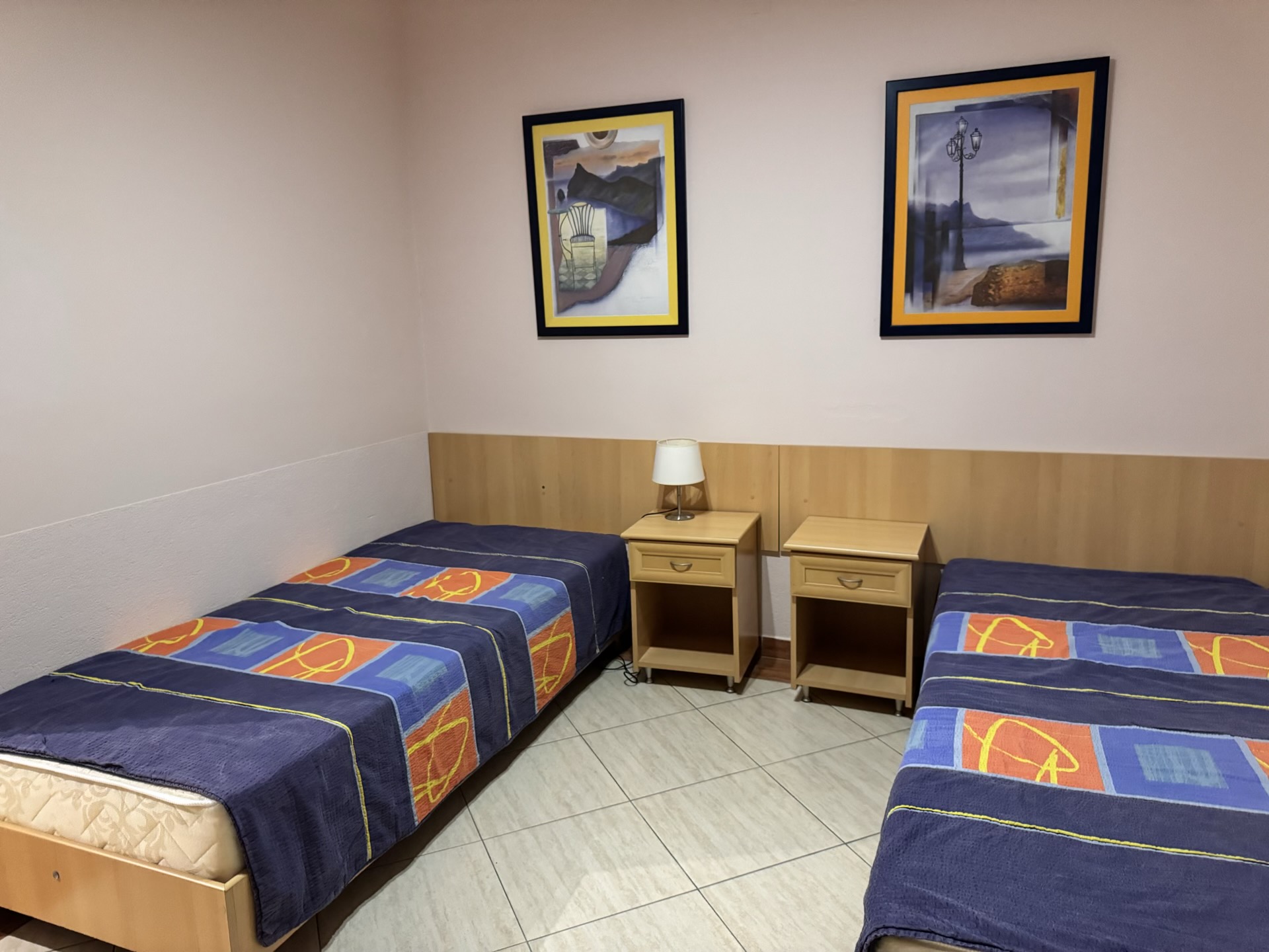 Schlafzimmer mit zwei Einzelbetten und Nachttischen in einer Wohnung in Budva, Montenegro. Innenraum mit Bildern an den Wänden.
