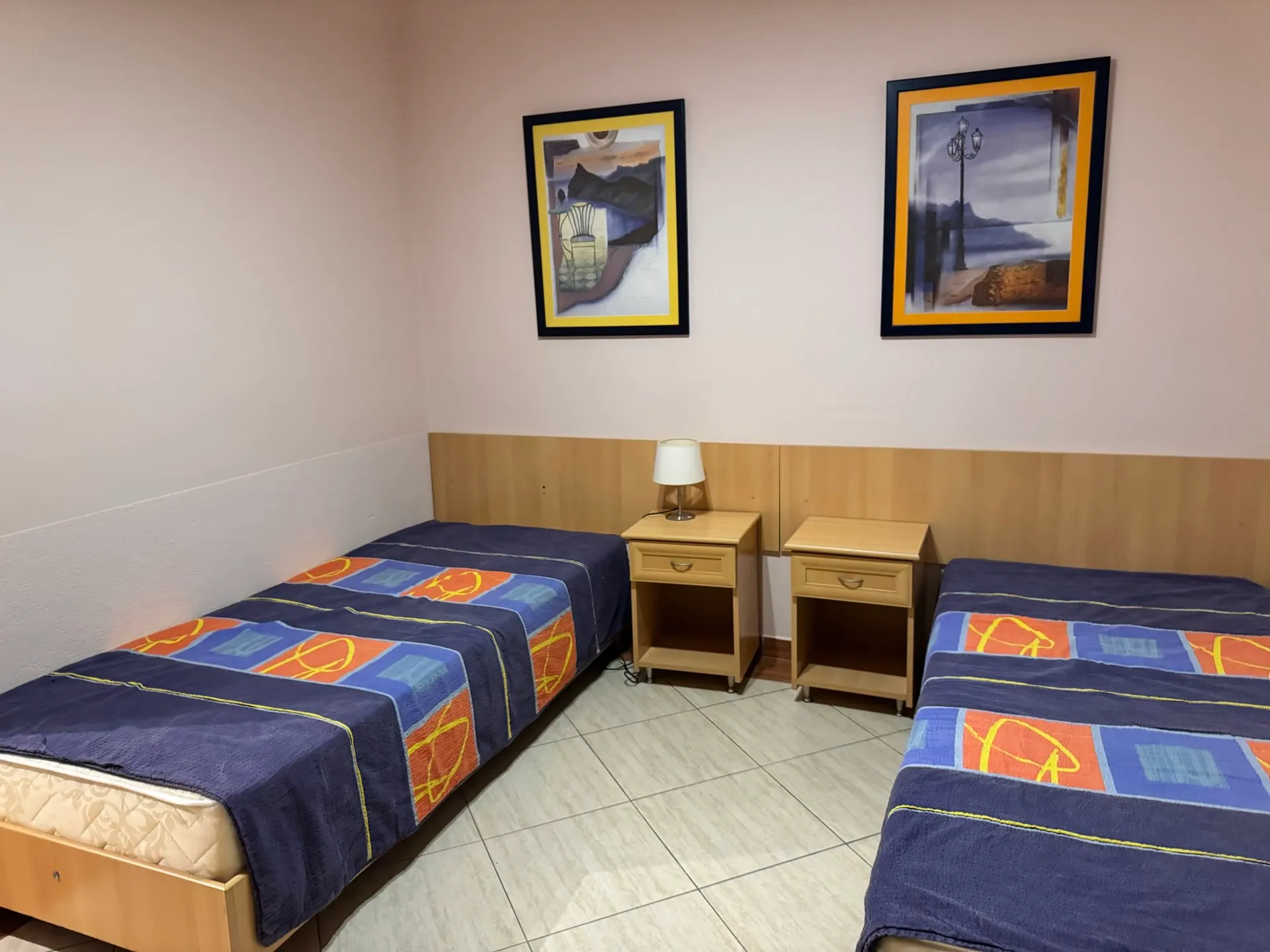 Bedroom with two single beds and bedside tables in an apartment in Budva, Montenegro. Interior with paintings on the walls.