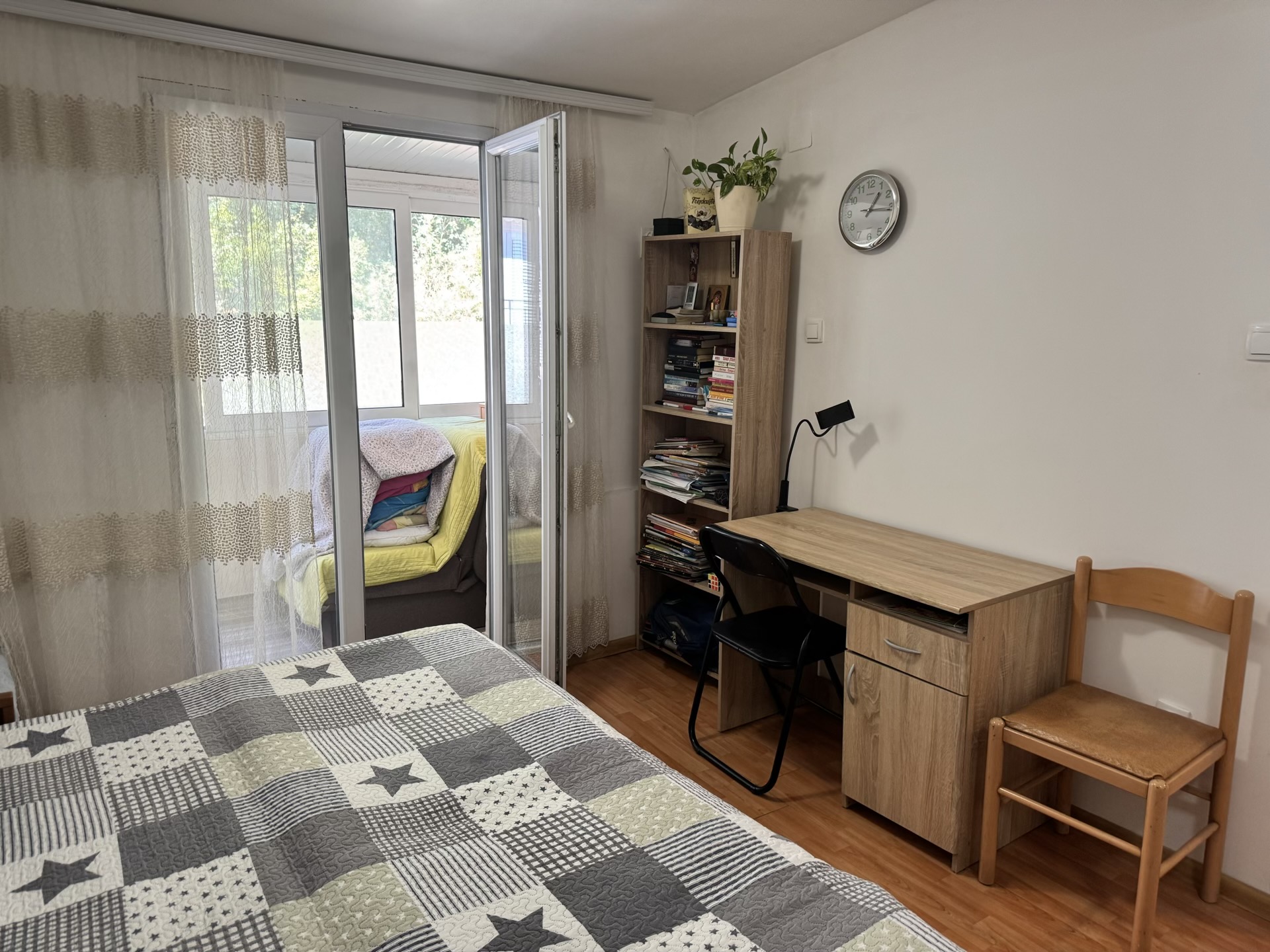 Schlafzimmer in einer Wohnung in Bečići, Montenegro: Bett mit gemusterter Tagesdecke, Schreibtisch, Regal und Zugang zum Balkon.