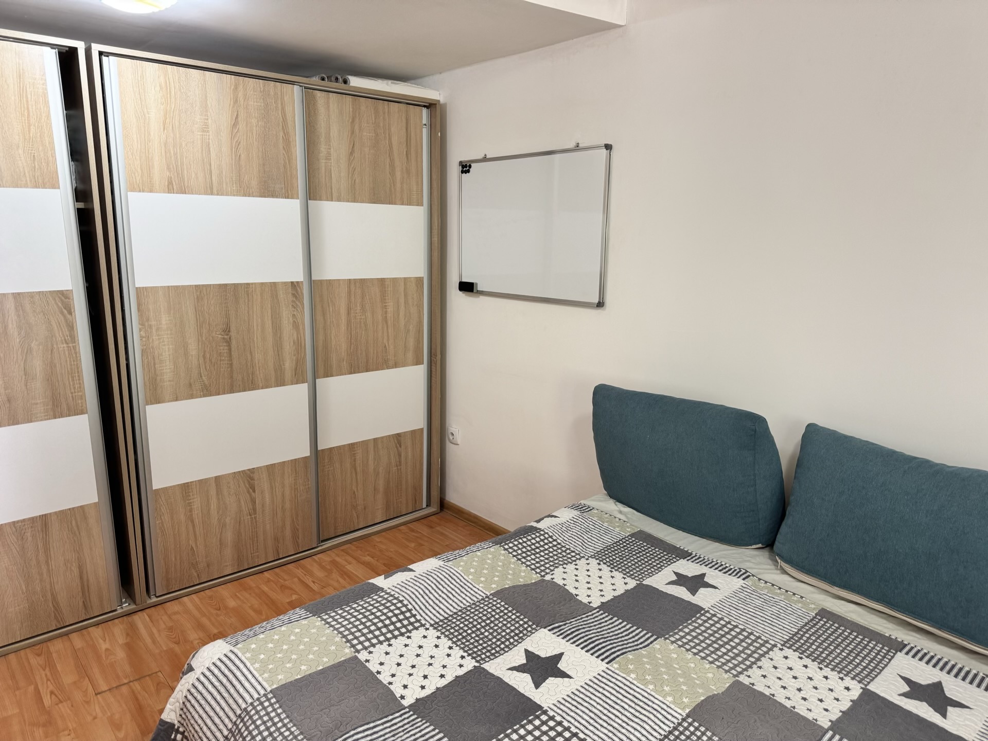 Schlafzimmer in einer Wohnung in Bečići, Montenegro: Doppelbett, Holzoptik-Schiebetürschrank und Whiteboard an der Wand.
