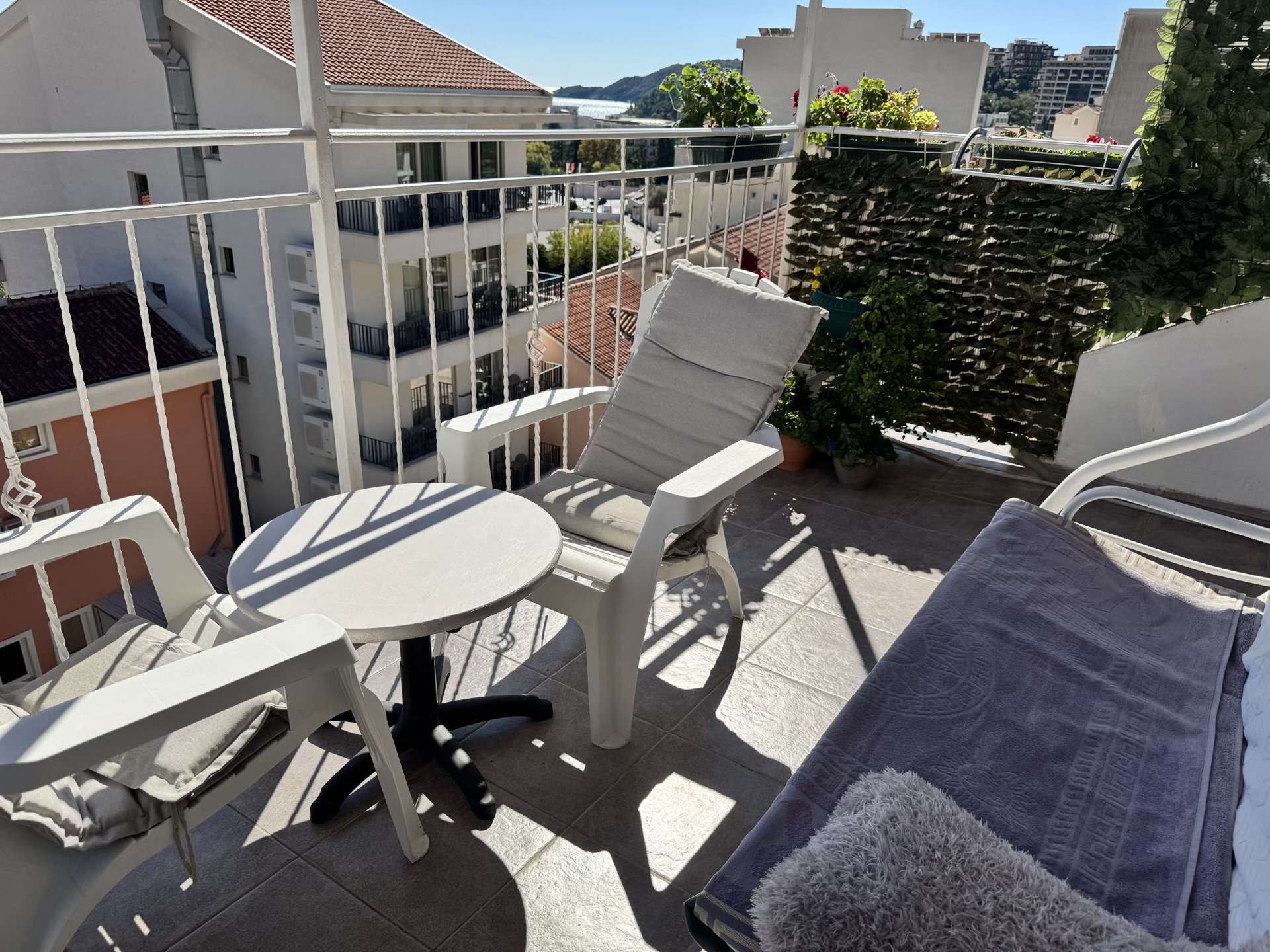 Gemütlicher Balkon mit Möbeln und Stadtblick in einer Wohnung in Bečići, Montenegro: Tisch, Sessel und Zimmerpflanzen.