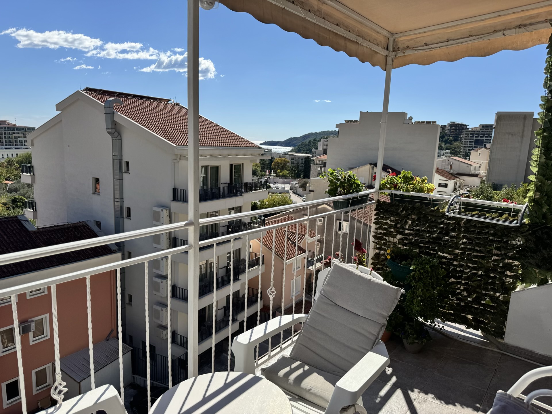 Balkon mit Möbeln und Blick auf das Meer und die Berge in einer Wohnung in Bečići, Montenegro. Gemütliche Terrasse mit Überdachung und Grünpflanzen.