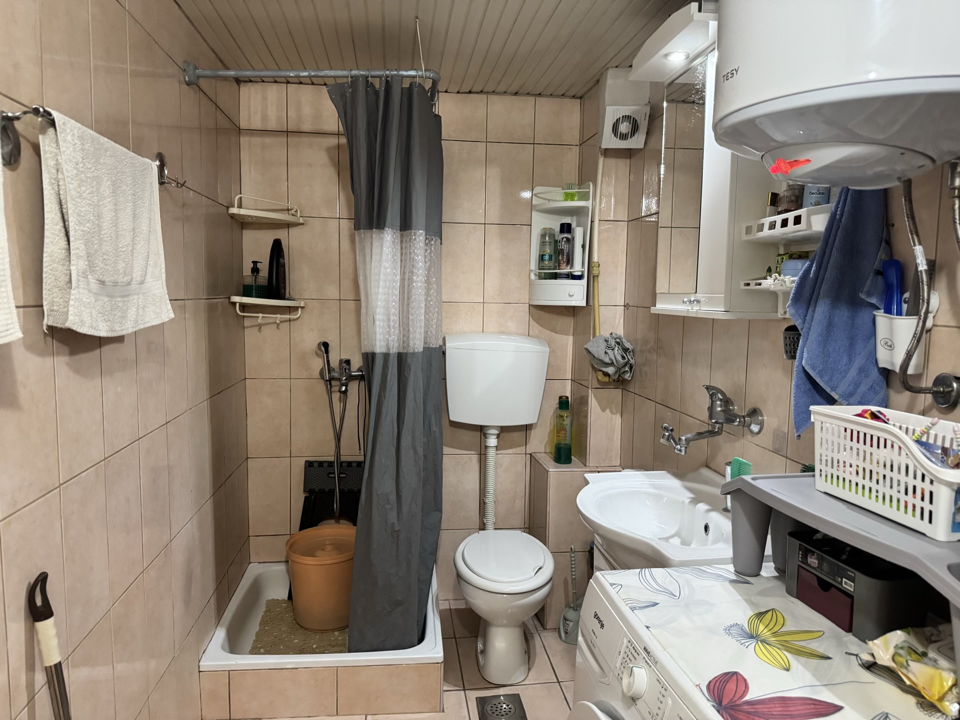 Badezimmer in einer Wohnung in Bečići, Montenegro: Fliesen, Duschbereich mit Vorhang, Toilette und Waschmaschine.