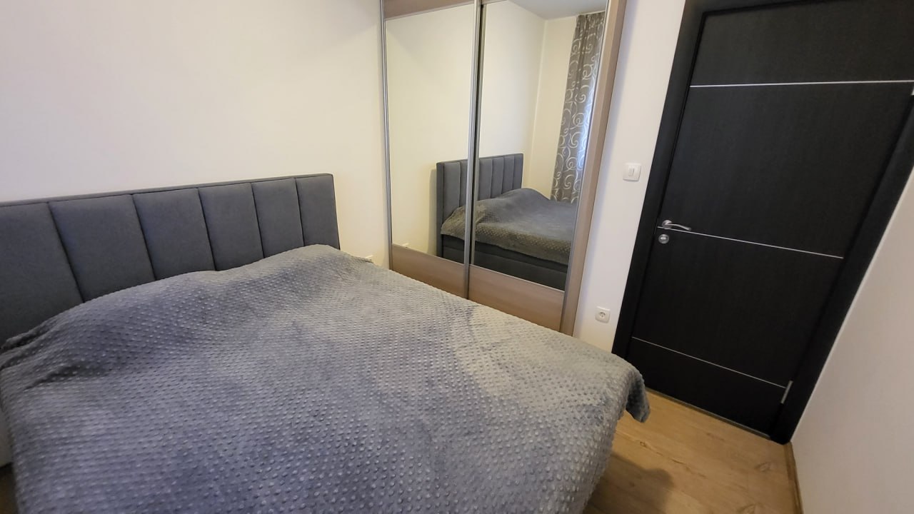 Schlafzimmer in einer Wohnung in Bečići, Montenegro: Doppelbett mit gepolstertem Kopfteil und Spiegel-Schiebetürschrank.