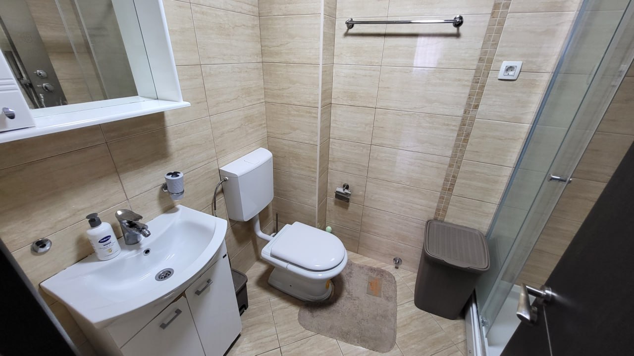 Modernes Badezimmer in einer Wohnung in Bečići, Montenegro: weiße Sanitärkeramik, Duschkabine und beige Fliesen.