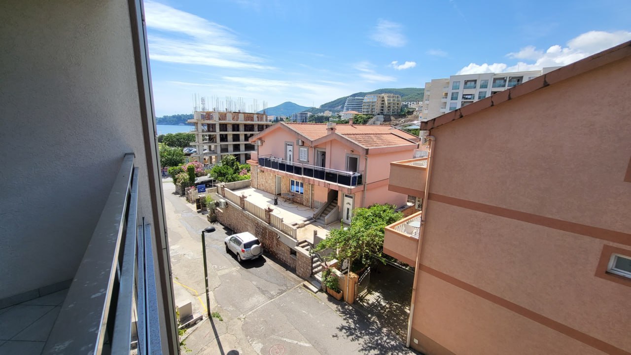 Blick vom Balkon der Wohnung in Bečići, Montenegro: Panorama auf die Nachbarhäuser, die Straße und die Küste in der Ferne.