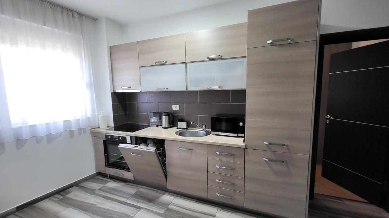 Moderne Küche in einer Wohnung in Bečići, Montenegro: helle Einbauküche, integrierte Geräte und dunkler Spritzschutz.