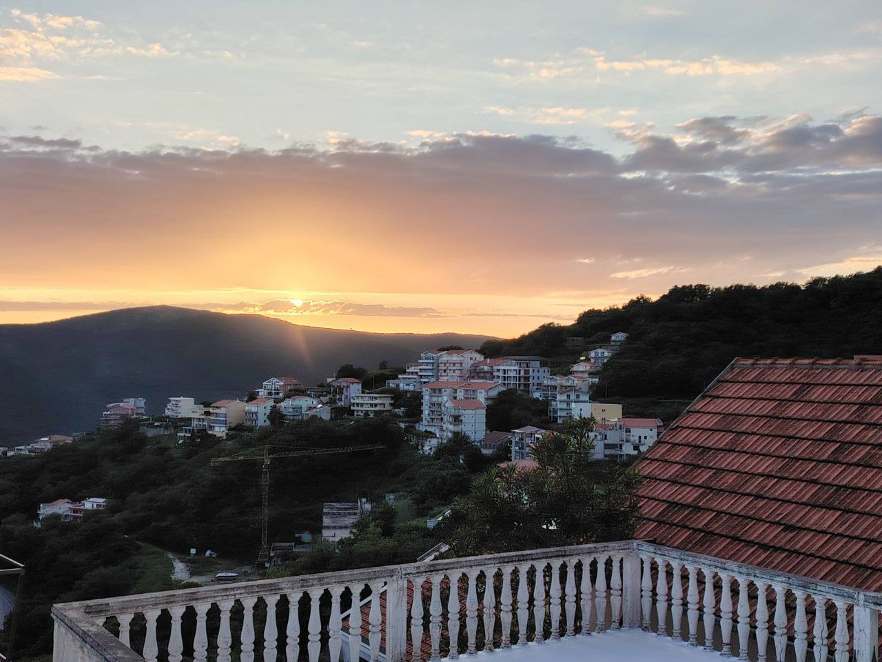 Vue depuis le balcon sur le coucher de soleil et les montagnes à Sutomore, Monténégro : panorama de la ville aux toits de tuiles et terrasse avec balustrade.