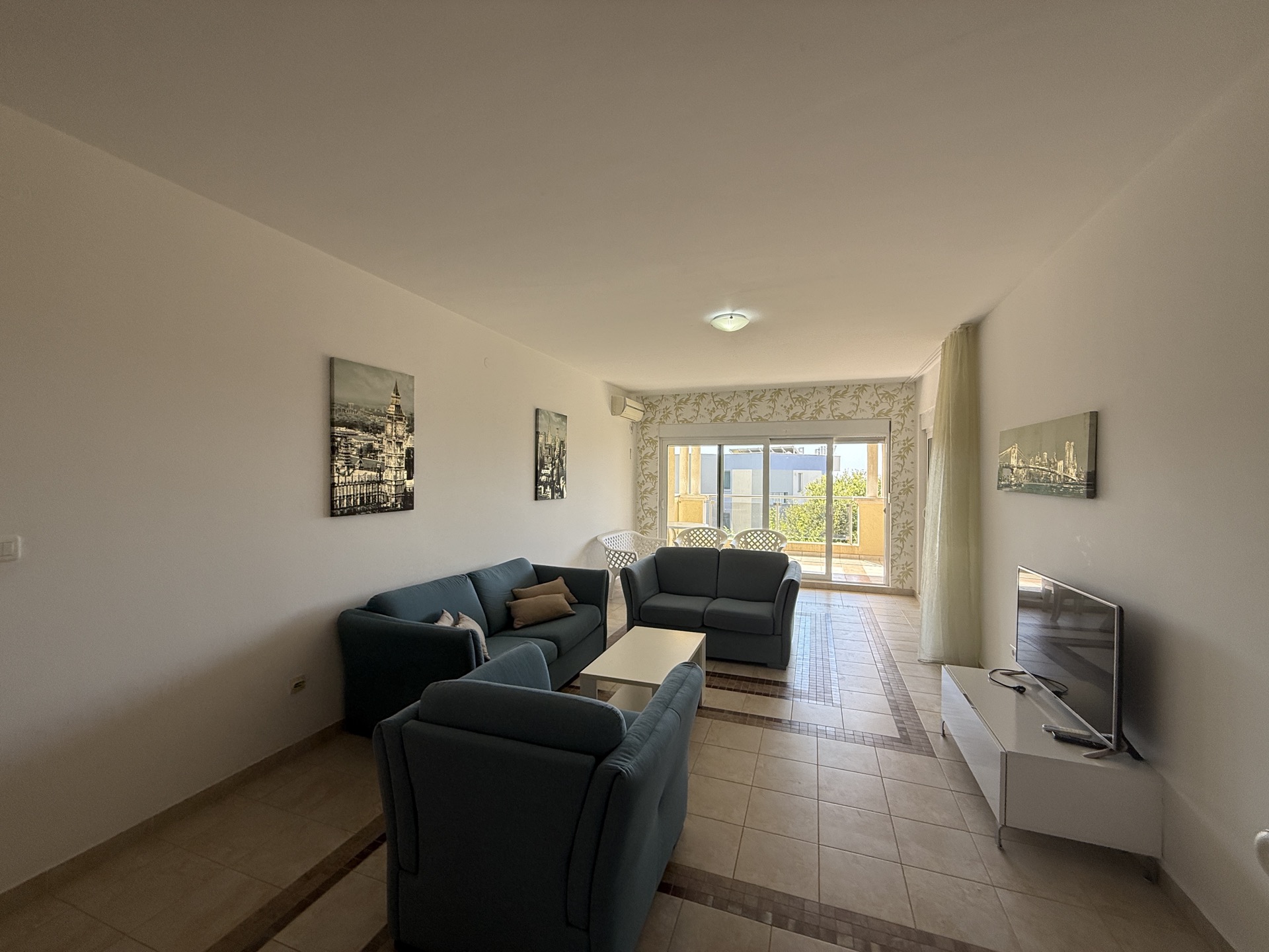Jasny salon z niebieskimi sofami i wyjściem na taras w apartamencie w Budvie, Czarnogóra. Podłoga z płytek, nowoczesny styl.