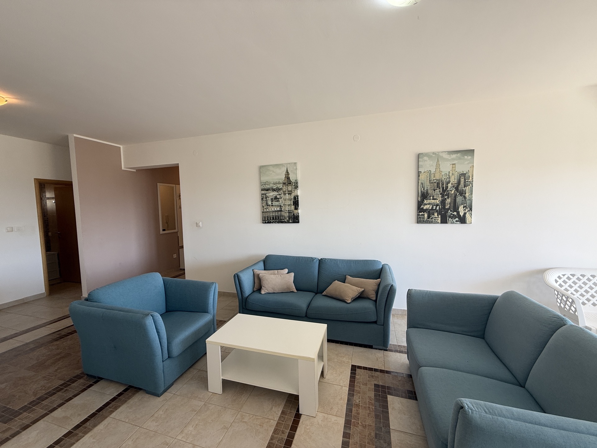 Jasny salon z niebieskimi meblami tapicerowanymi w mieszkaniu na sprzedaż w Budvie, Czarnogóra: sofy, fotel i stolik kawowy.