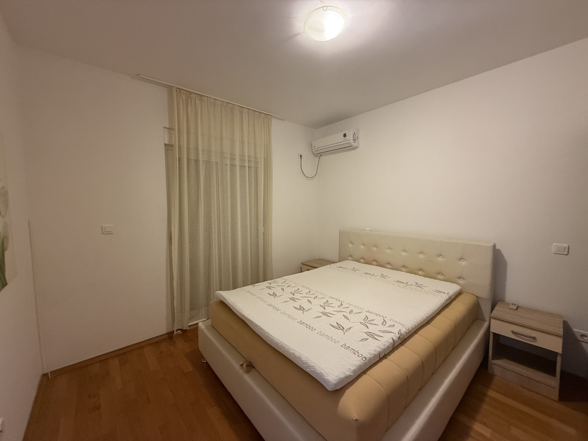 Jasna sypialnia z łóżkiem dwuosobowym i klimatyzacją w mieszkaniu w Budvie, Czarnogóra, z wyjściem na balkon.