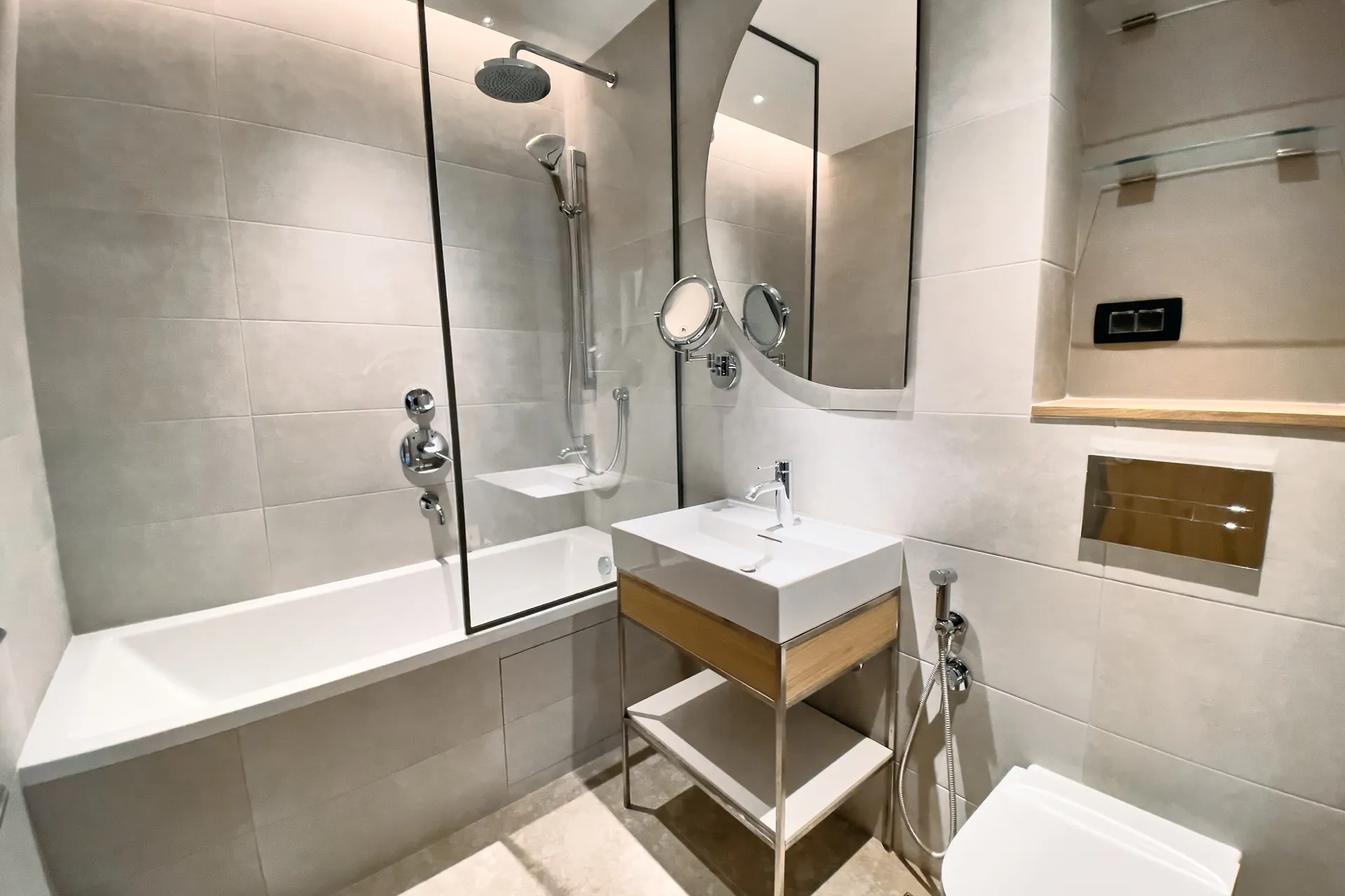 Moderne Badezimmer mit weißer Badewanne, Duschsystem, wandmontierter Toilette und Waschtisch auf einem Holzwaschtisch.