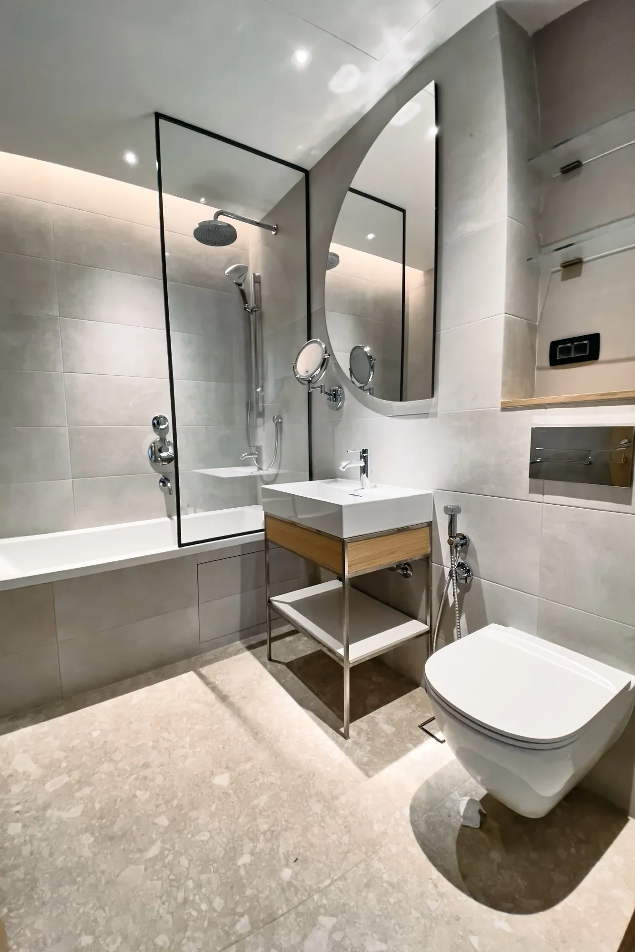 Moderne Badezimmer mit grauen Fliesen, wandmontierter Toilette, Holzwaschtisch und einer Duschkabine aus Glas.