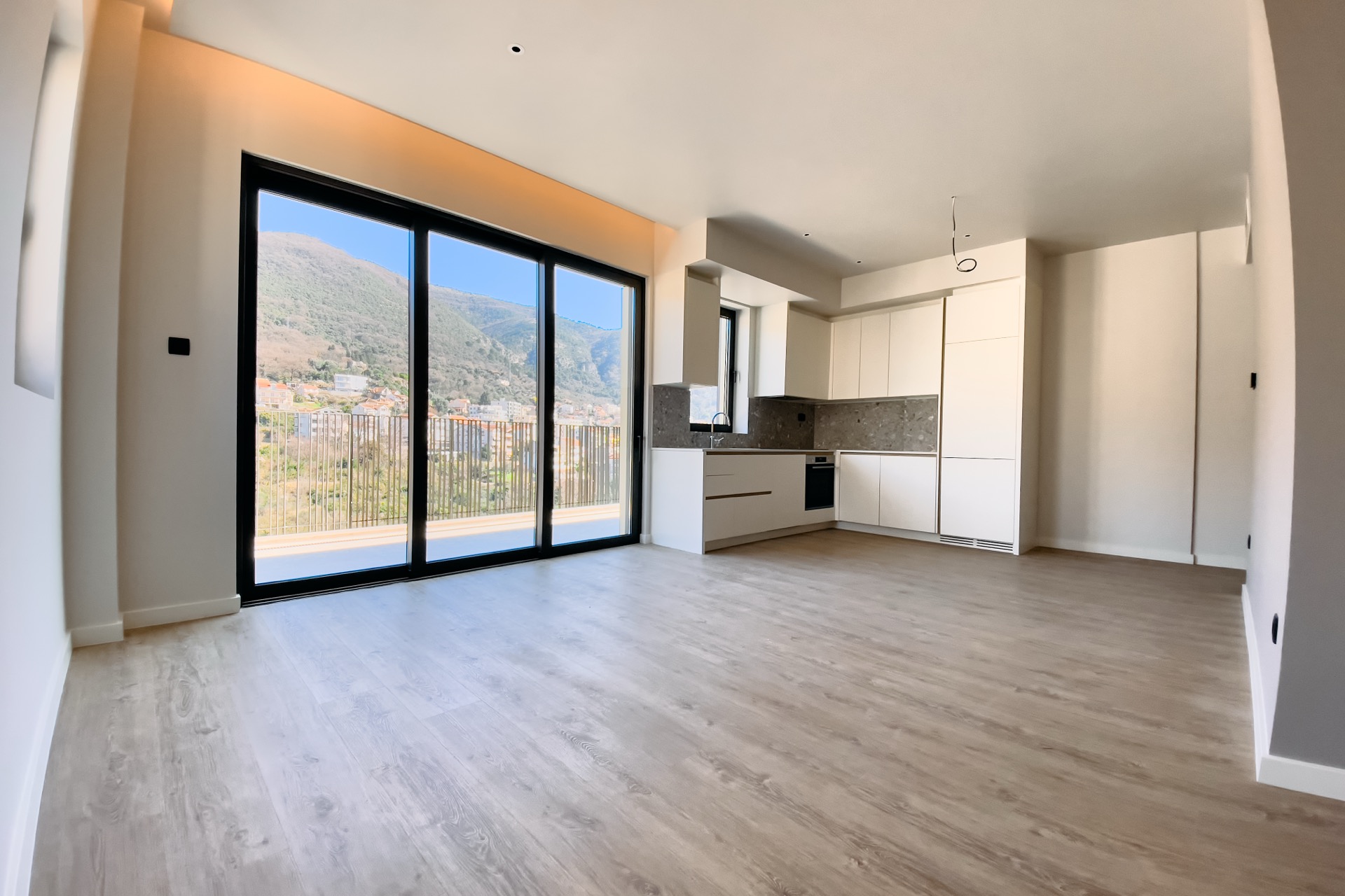 Modernes Wohnzimmer mit Küche in einer Wohnung, Tivat, Montenegro: Panoramafenster mit Bergblick und helle Ausstattung.