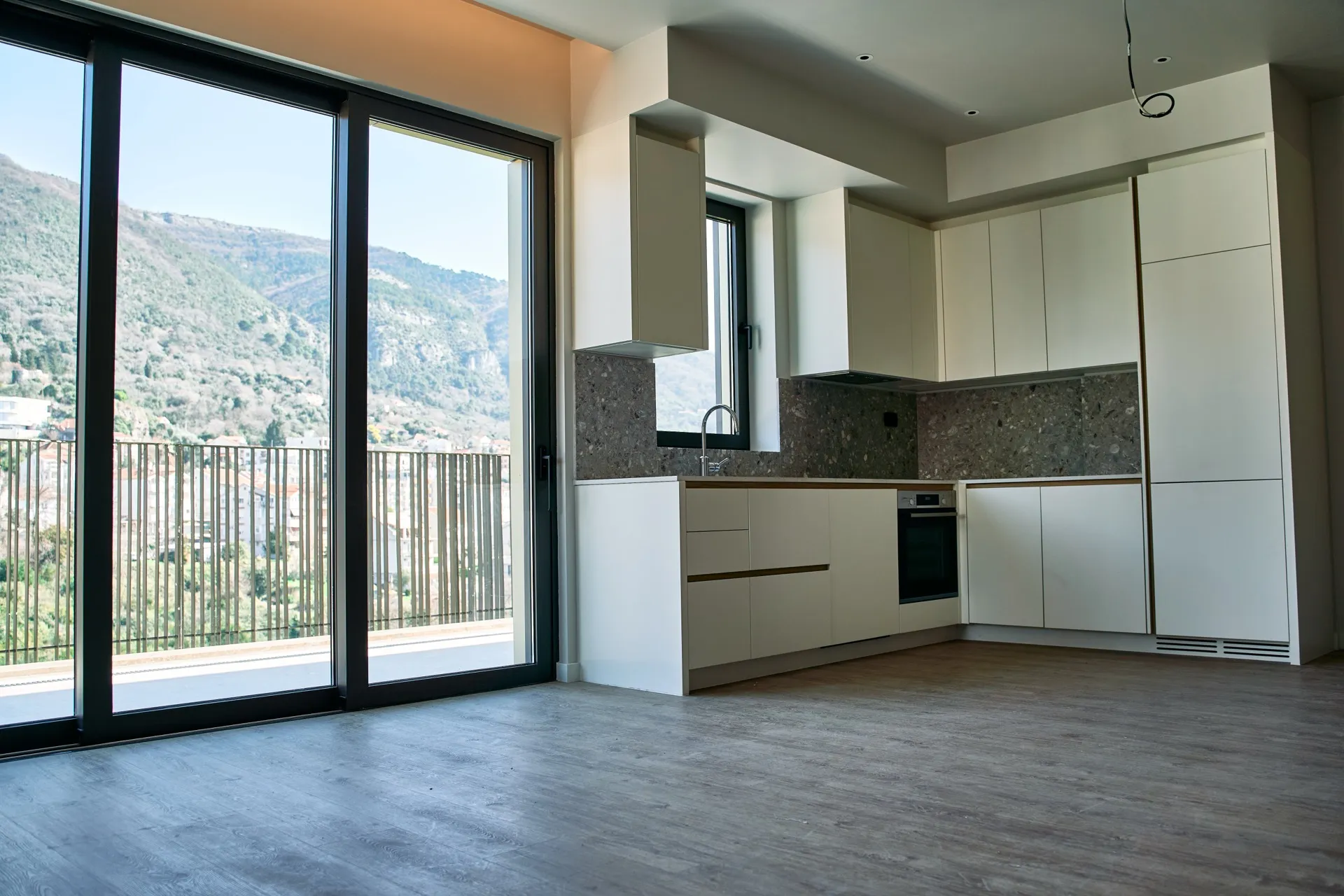 Moderne Küche mit weißen Schränken, grauer Arbeitsfläche und großem Fenster mit Bergblick.
