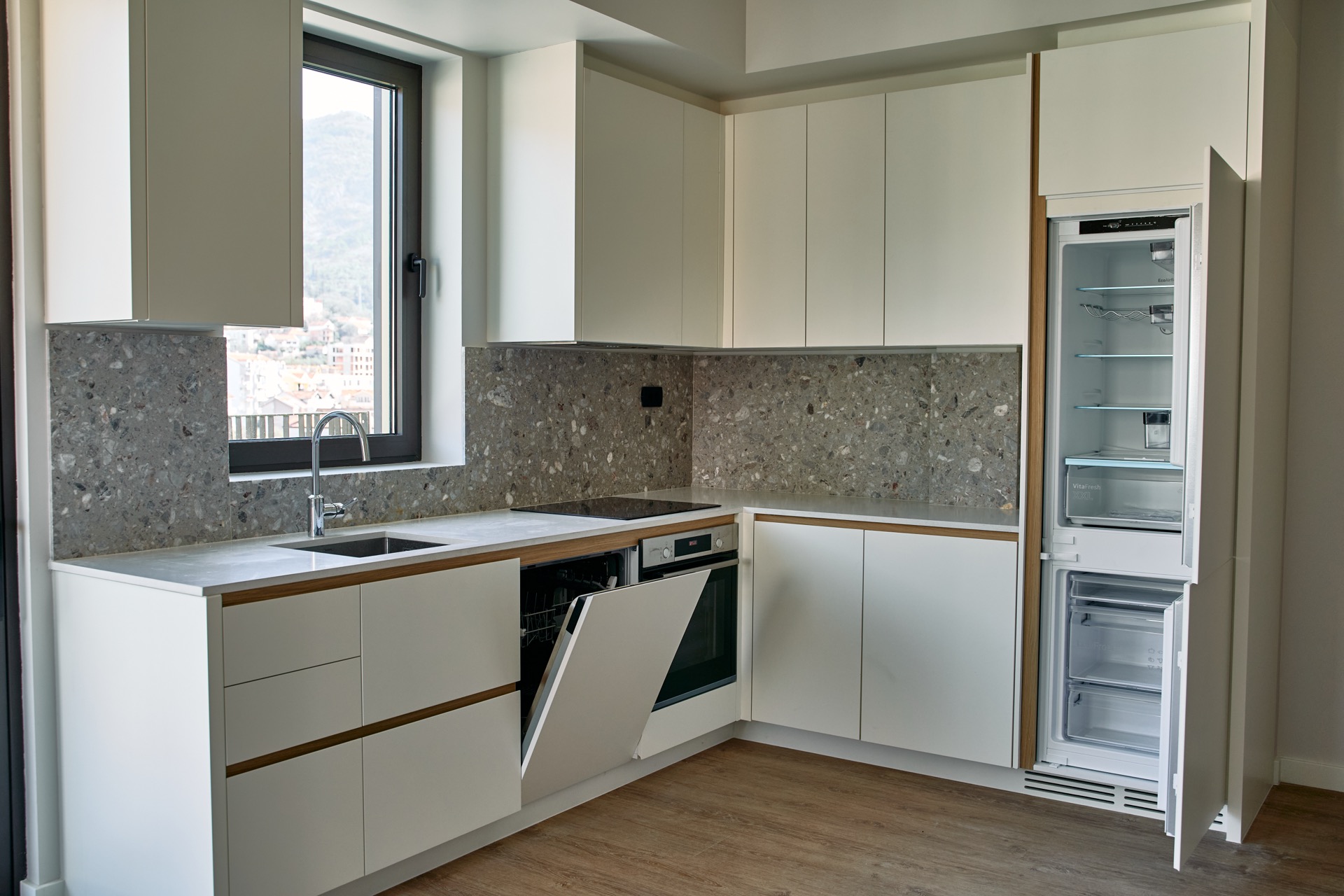 Moderne Küche in einer Wohnung, Tivat, Montenegro: Einbaugeräte, Steinrückwand und Bergblick aus dem Fenster.