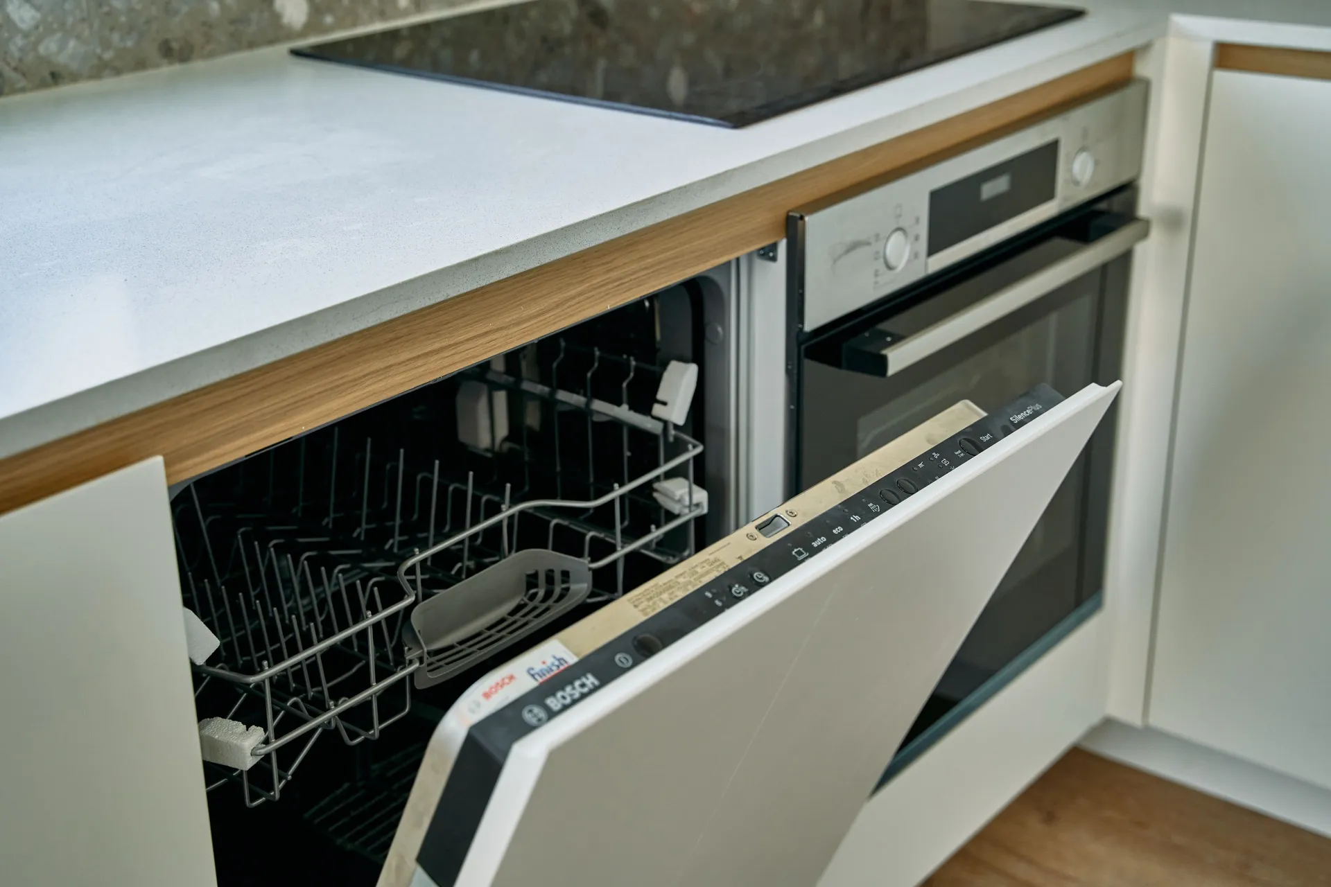 Eine offene integrierte Bosch-Spülmaschine ist neben einem Backofen unter einer hellen Arbeitsplatte in einer Küche sichtbar.