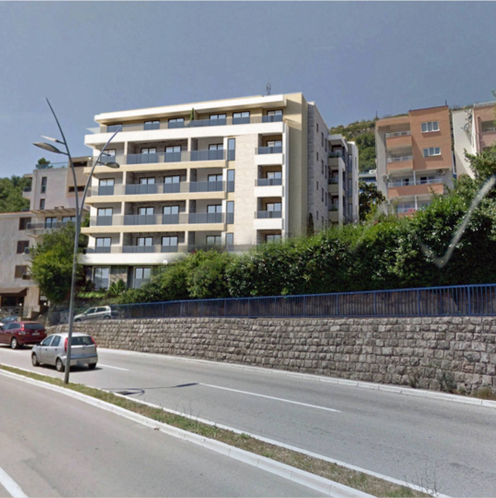 Moderner Wohnkomplex mit Balkonen in Bečići, Montenegro: Blick auf die Fassade des Gebäudes an der Straße mit einer Stützmauer aus Naturstein