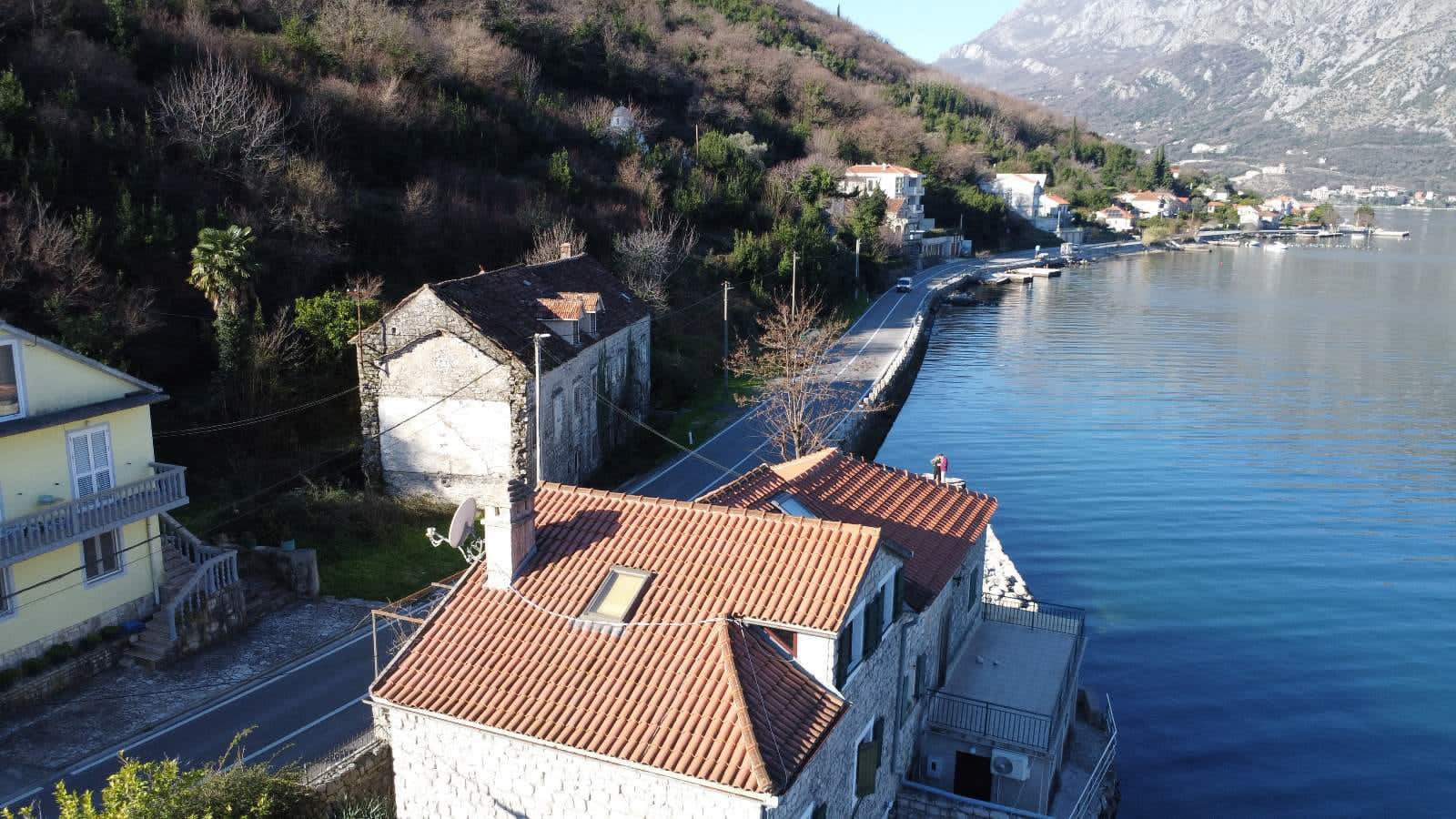 Steinhaus mit Ziegeldach in erster Meereslinie in Kostanjica, Montenegro: Luftaufnahme der Küste und Berge.