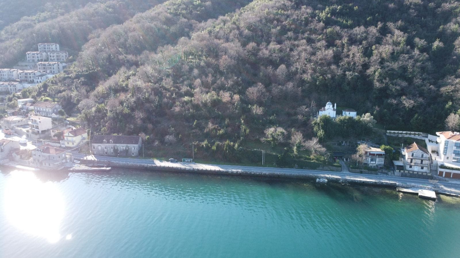 Luftaufnahme eines Küstengrundstücks und von Häusern in Kostanica, Montenegro: Panorama von Meer, Berghang und historischen Gebäuden.