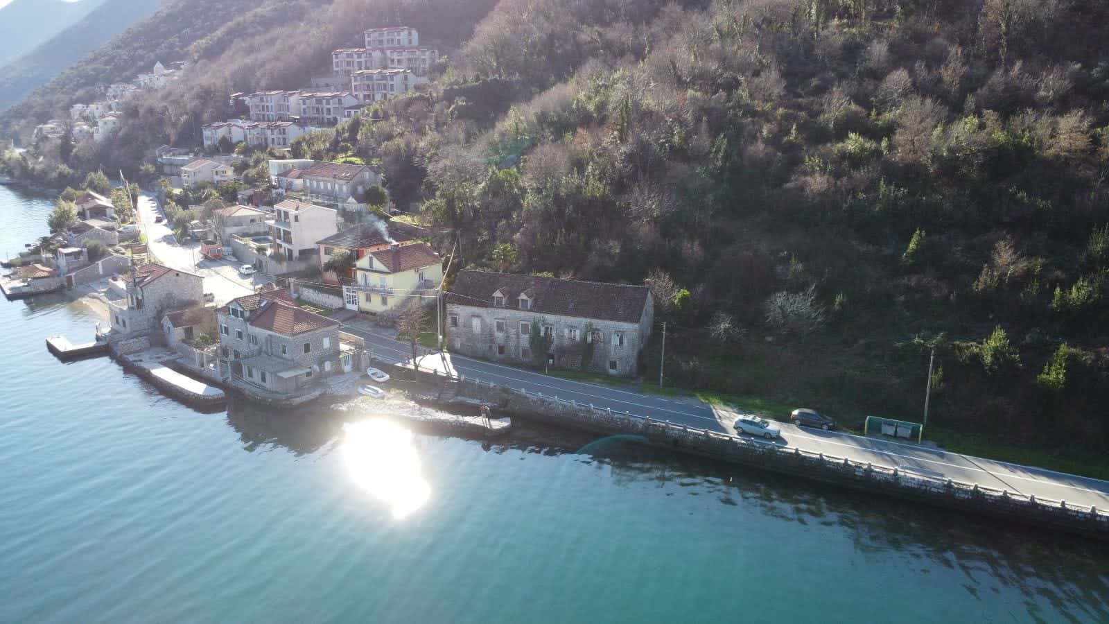 Luftaufnahme eines Steinhauses am Meer im Dorf Kostanica, Montenegro: Küstenlinie, Straße und Berglandschaft.